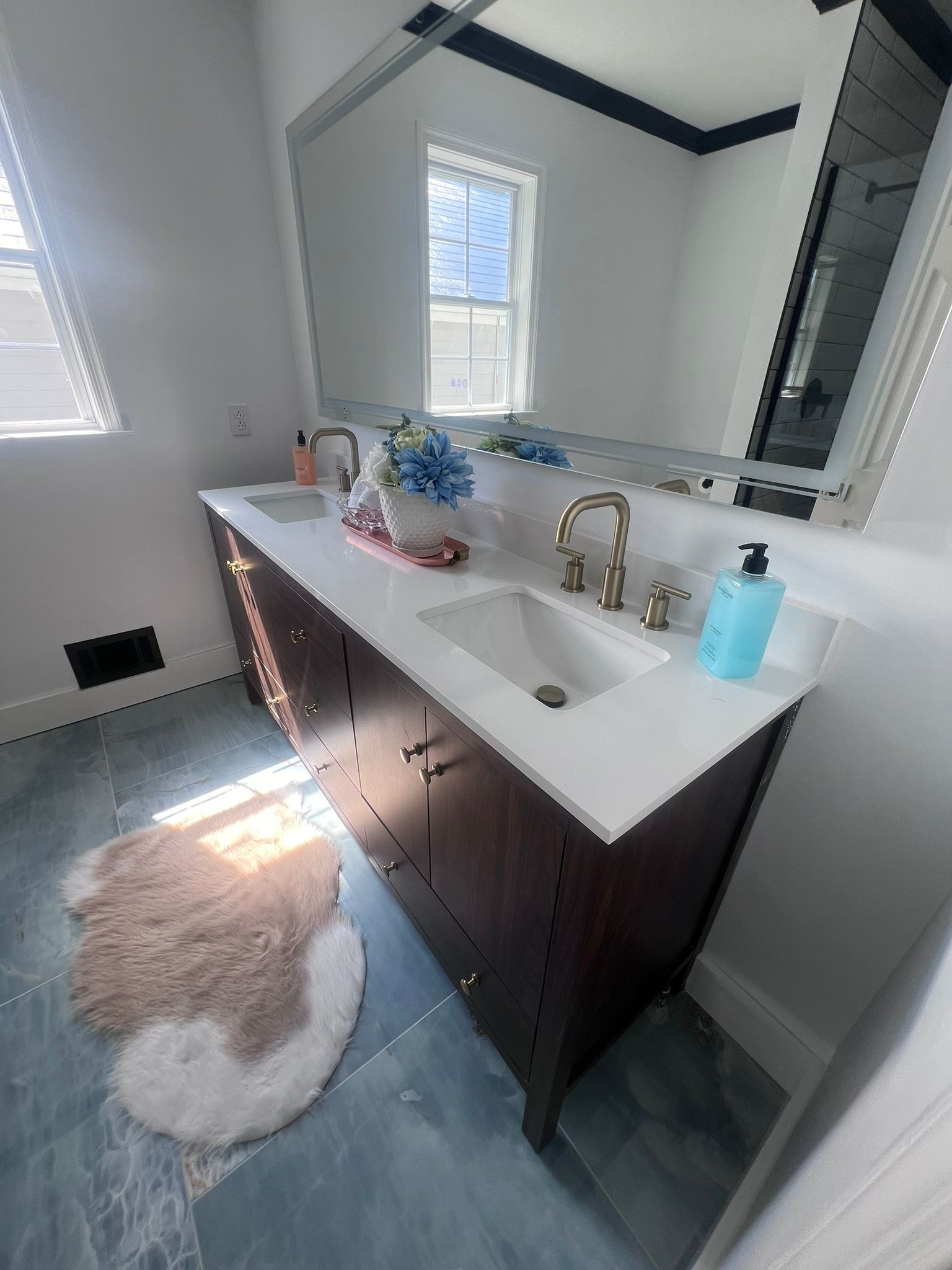 Bathroom with dark wood vanity, white countertop, gold fixtures, large mirror, and a small rug.