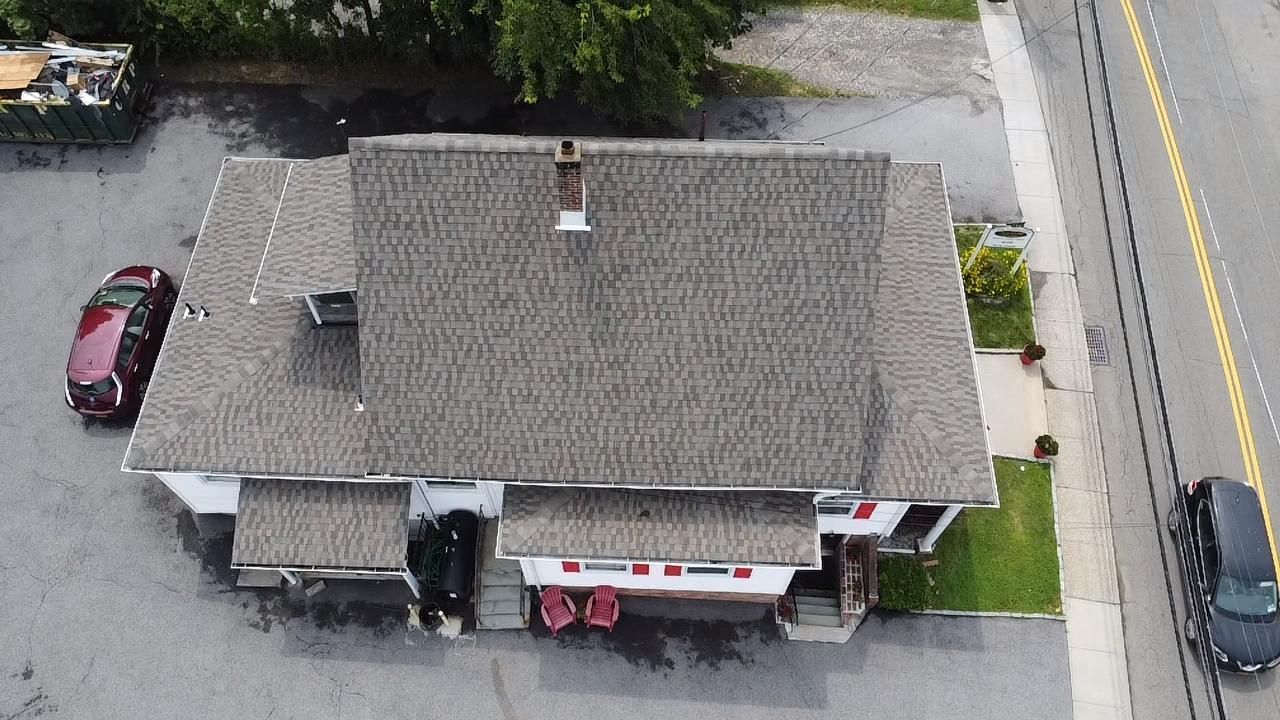 Overhead view of a building with a gray roof, red car, black car, and a road.