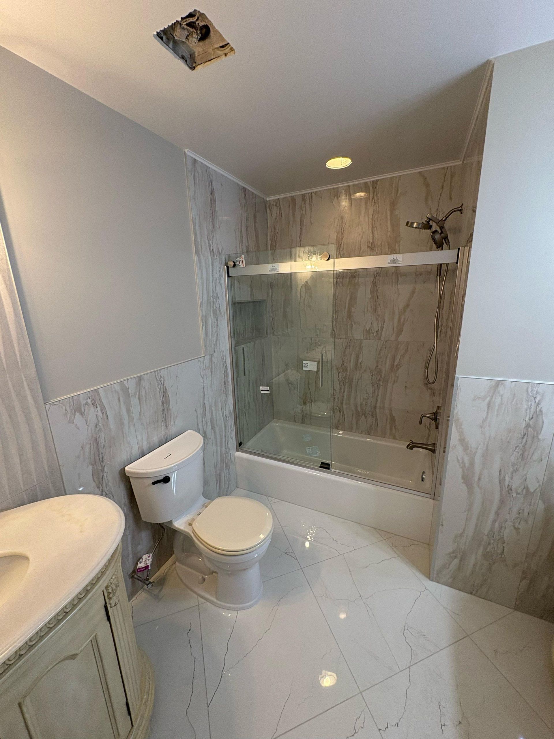 Bathroom with marble-like tile. Includes a toilet, vanity, and a shower with a glass door.