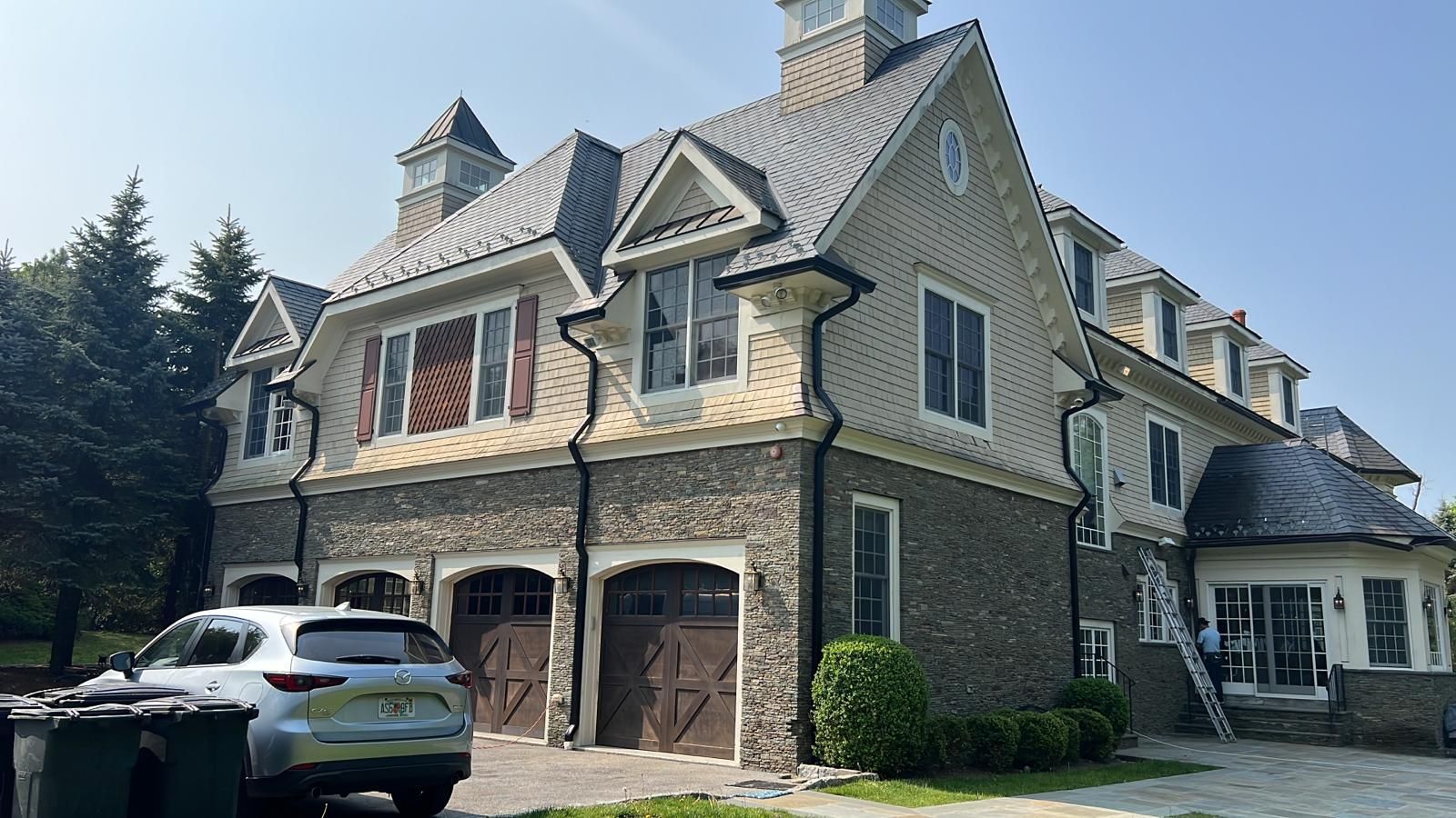 Multi-story house with stone and tan siding, brown garage doors, and a silver car parked outside.