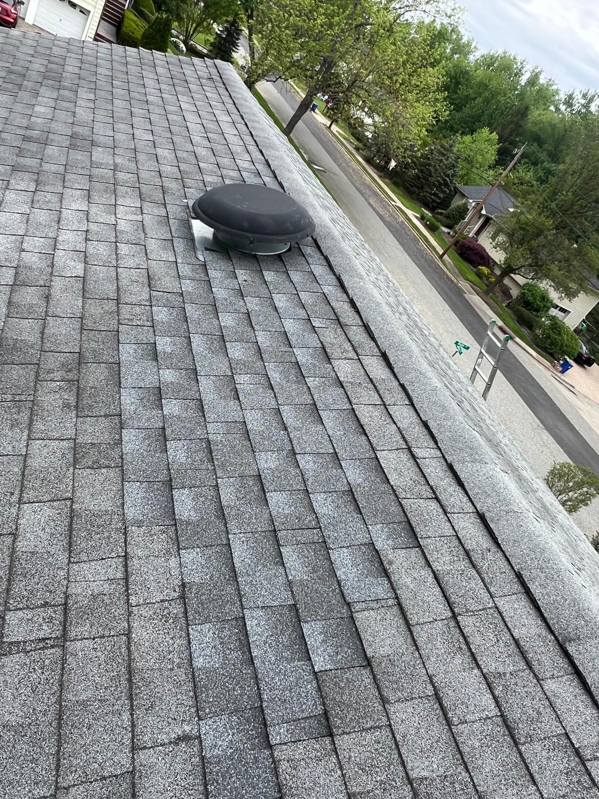 Gray asphalt shingle roof with a round, black vent in the center; residential setting.