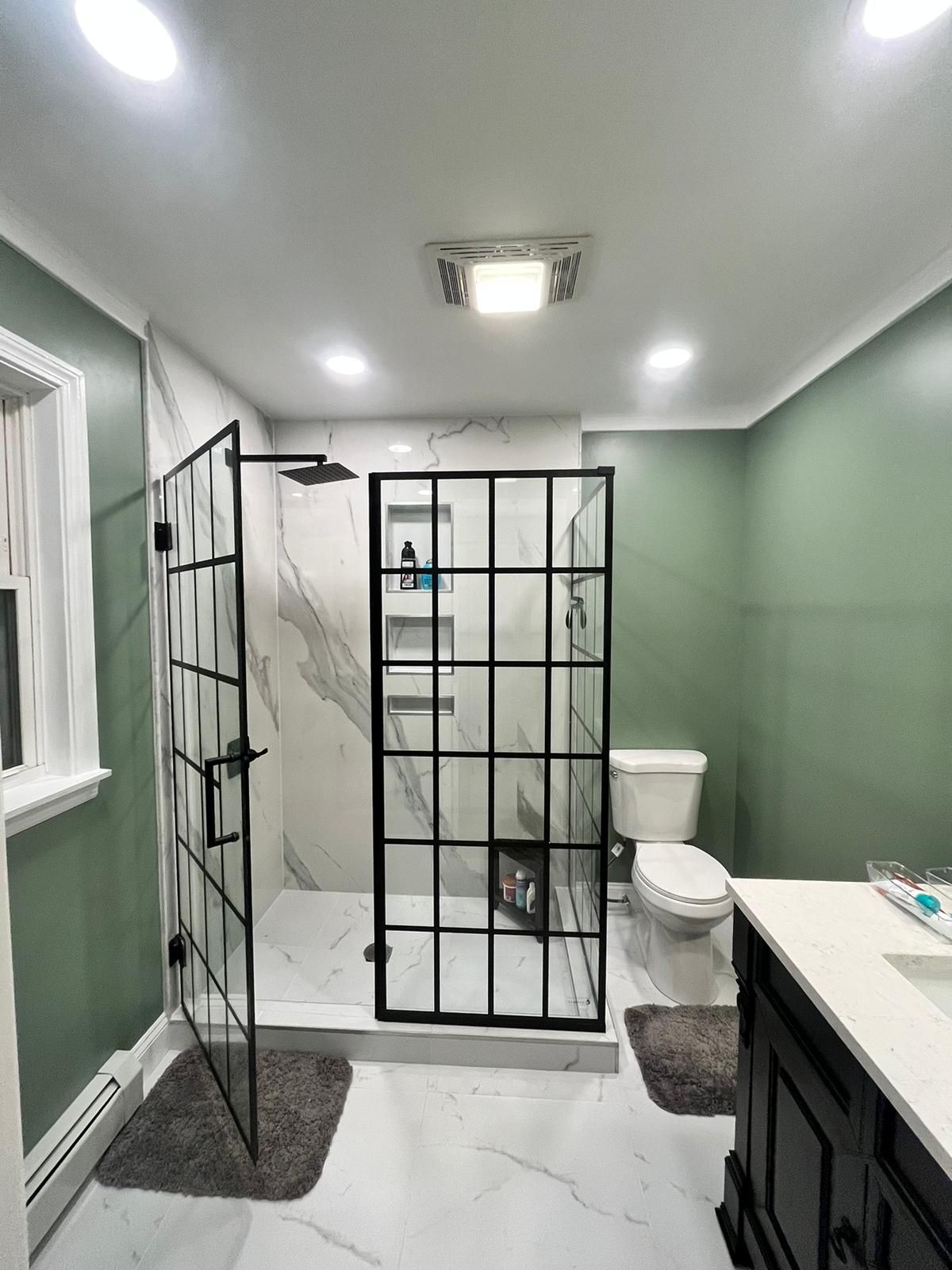 Modern bathroom with white marble tile and black framed shower. Green walls and a white toilet.
