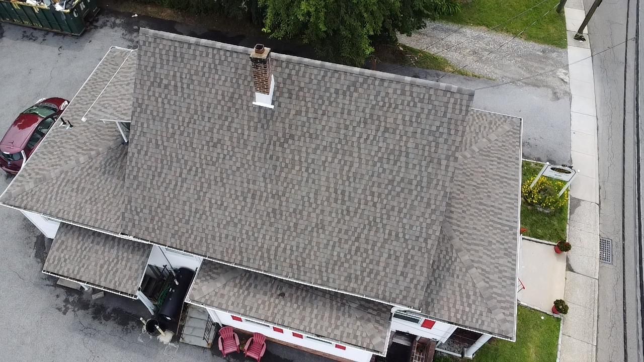 Overhead view of a house with a gray roof, chimney, and a road on the right.