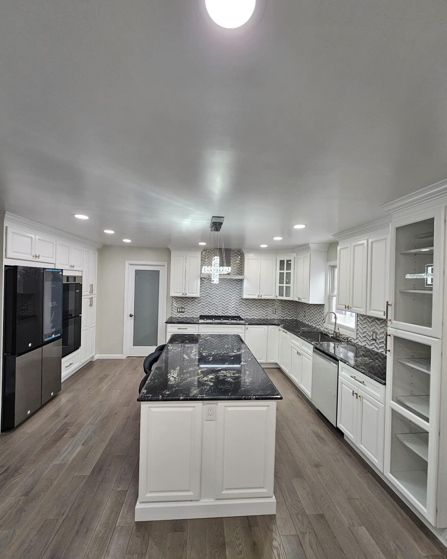 White kitchen with dark granite island. White cabinets, light wood floor, stainless steel appliances, and a glass door.