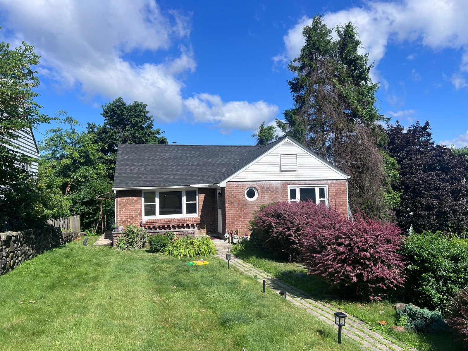 Brick house with dark roof, small yard, and walkway on a sunny day.