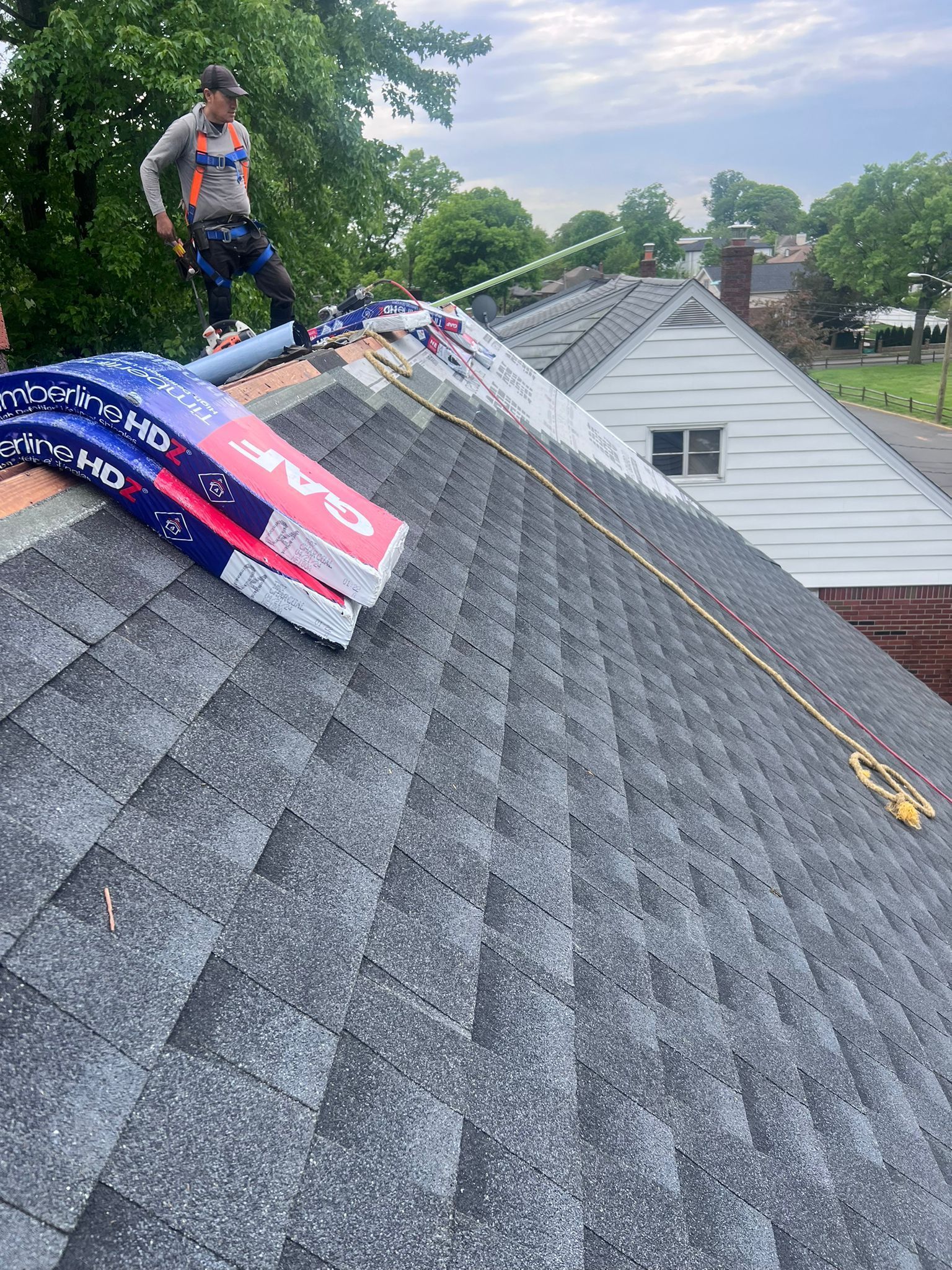 Roofer on a roof, preparing for work. Blue, red, and white roofing materials are nearby. Cloudy sky.