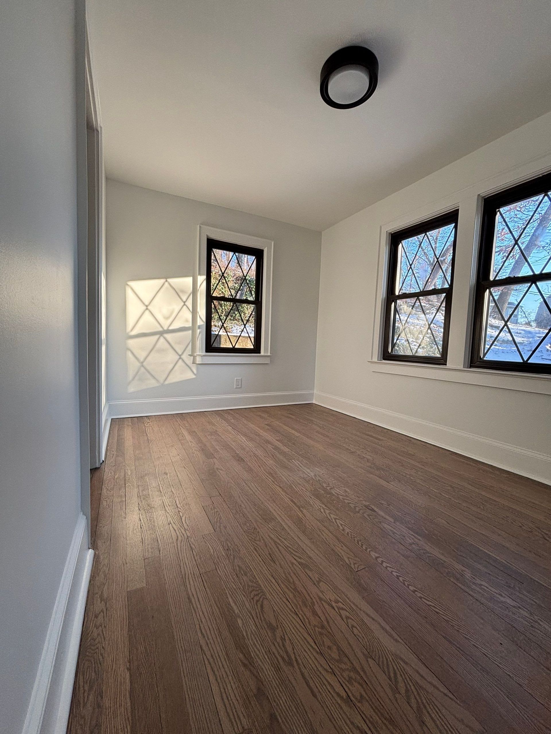 Empty room with hardwood floors, windows, and a ceiling light.