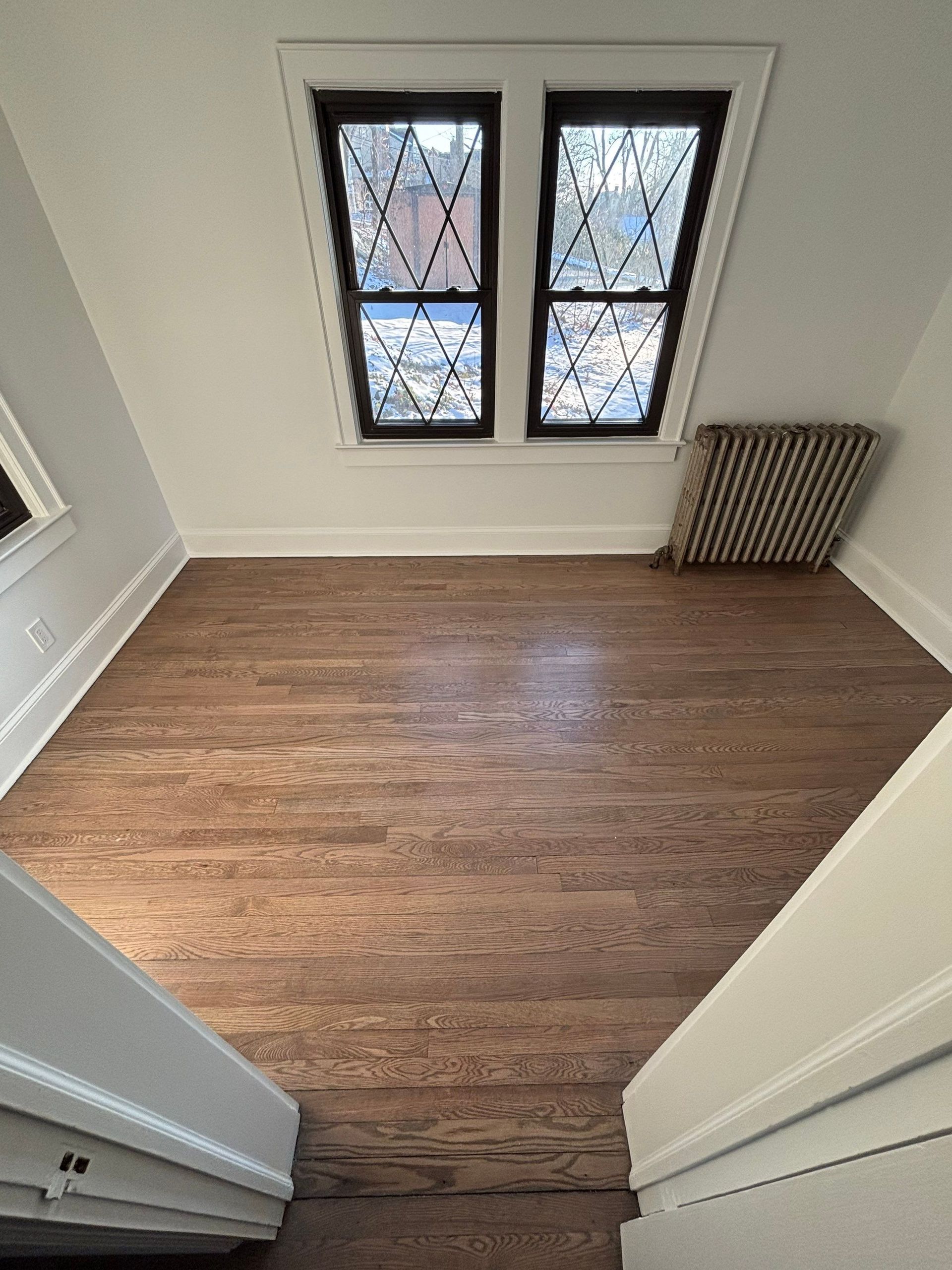 Empty room with angled walls, wooden floor, and a window with a diamond pattern.