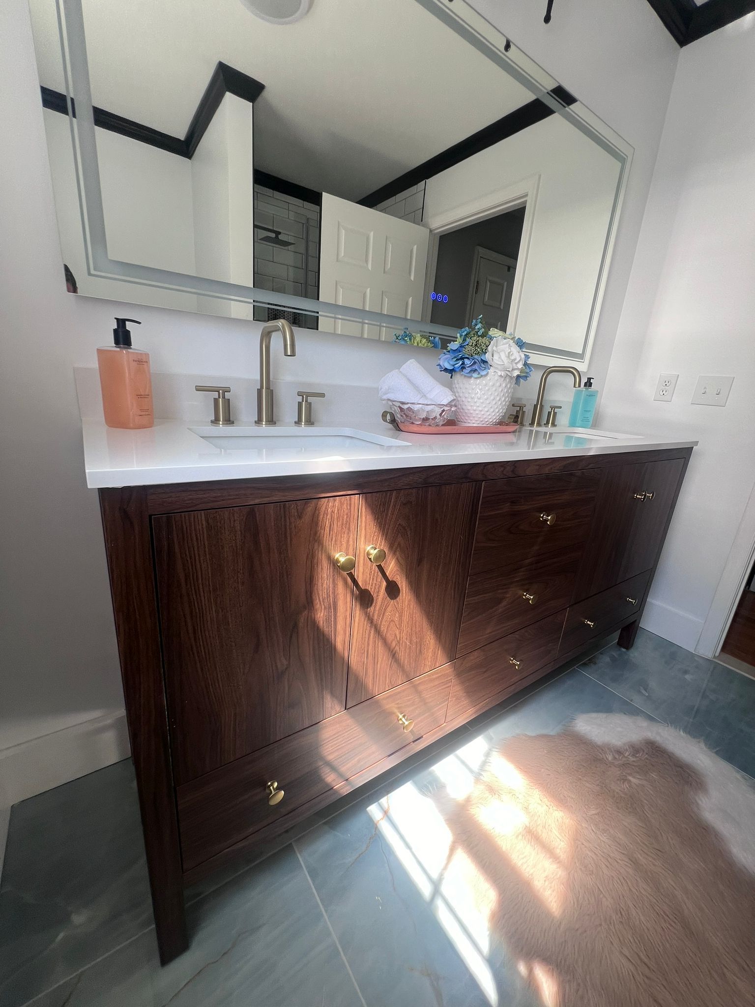 Dark wood bathroom vanity with white countertop, large mirror, and gold fixtures.