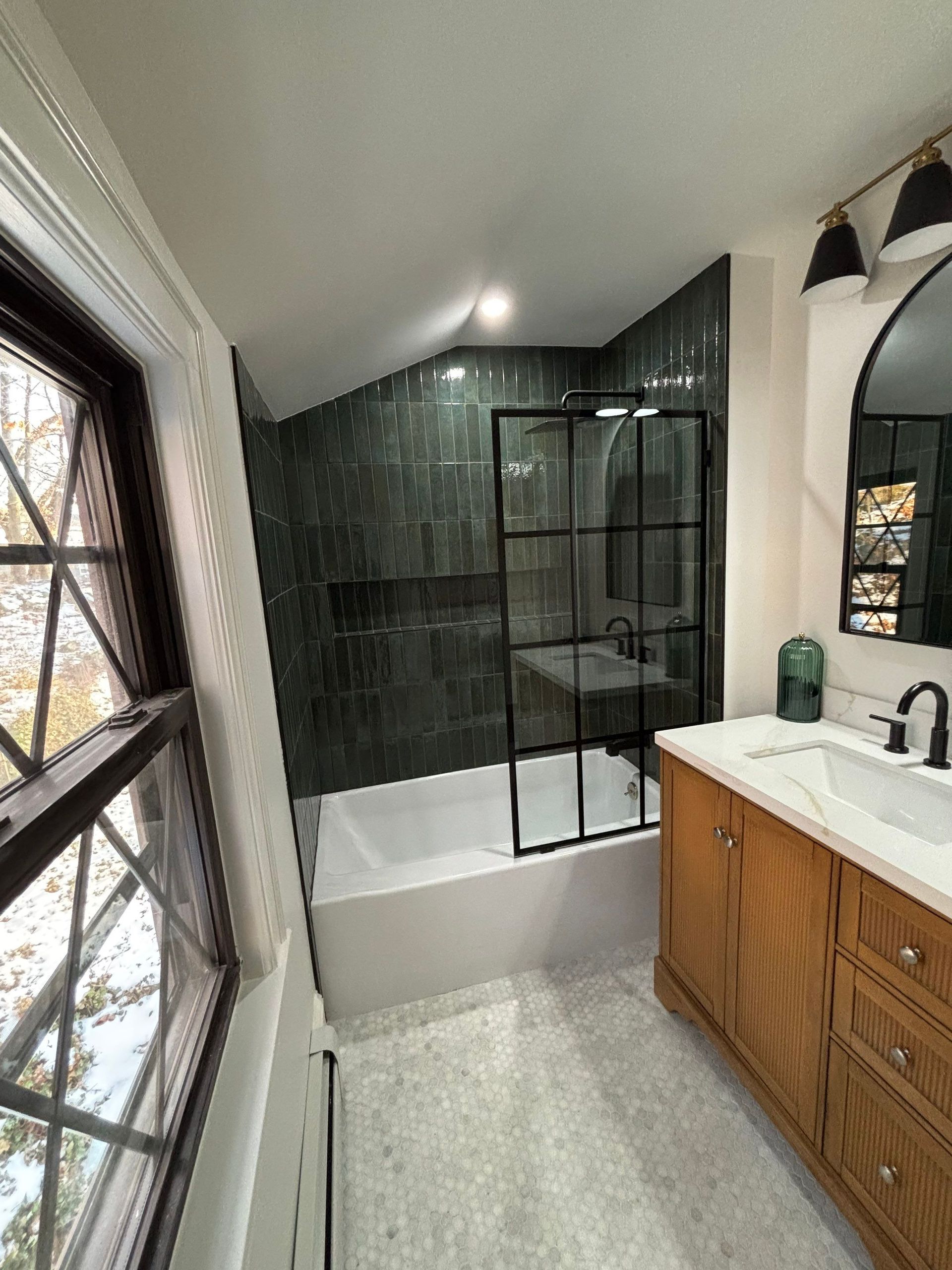 Bathroom with a black-framed shower, green tiled wall, wooden vanity, and a window.