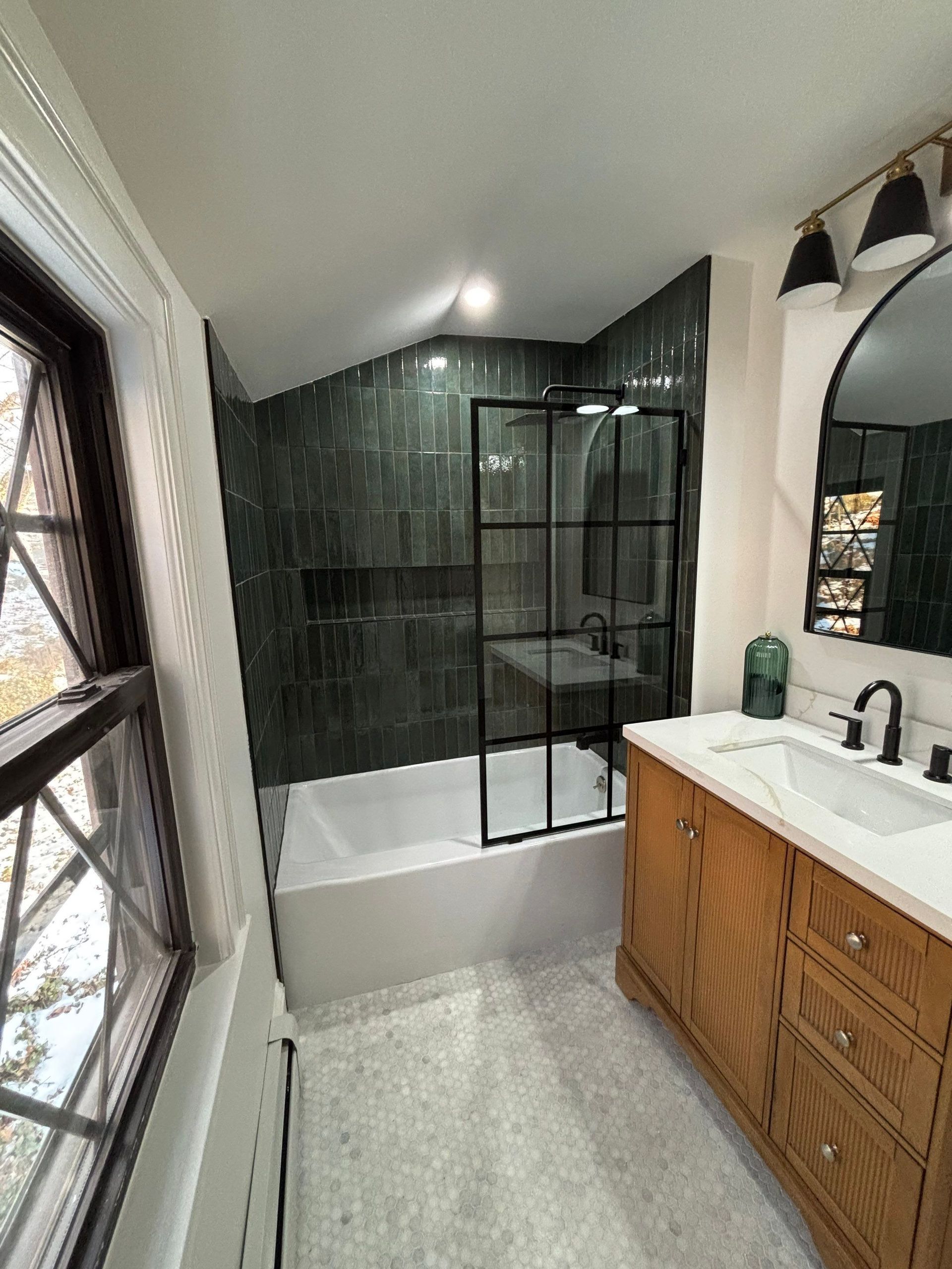 Bathroom with green tiled shower, white tub, wooden vanity, and large window.