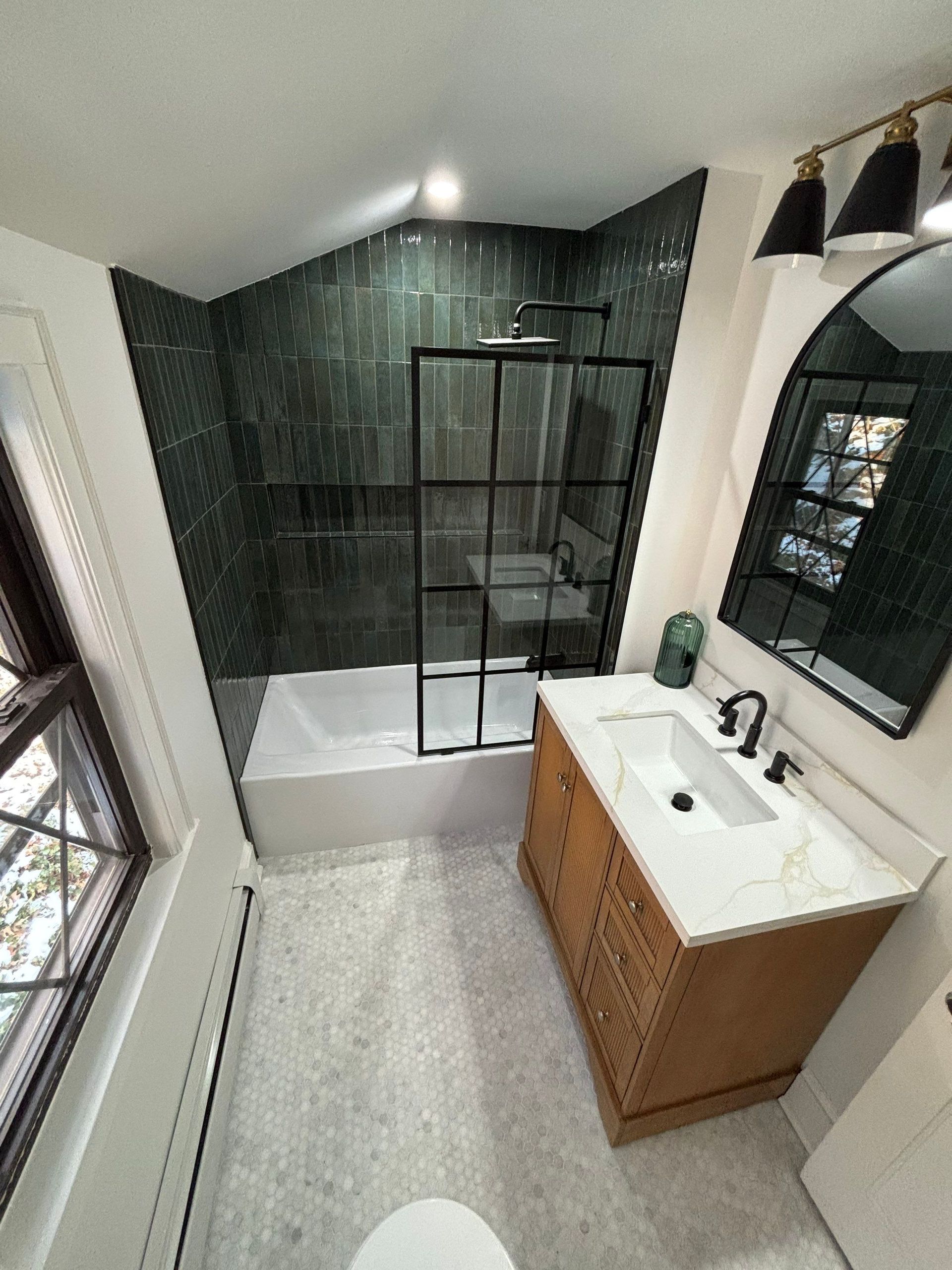 Bathroom with dark green tiled shower, black fixtures, wooden vanity, and marble countertop.