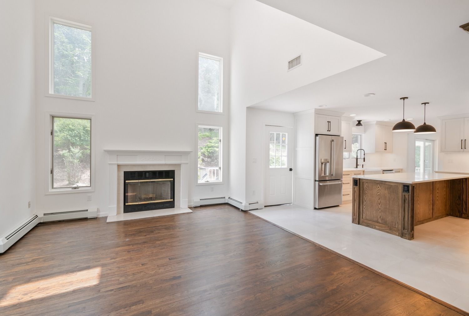 Spacious open-concept living room with fireplace and kitchen, featuring hardwood floors and white walls.