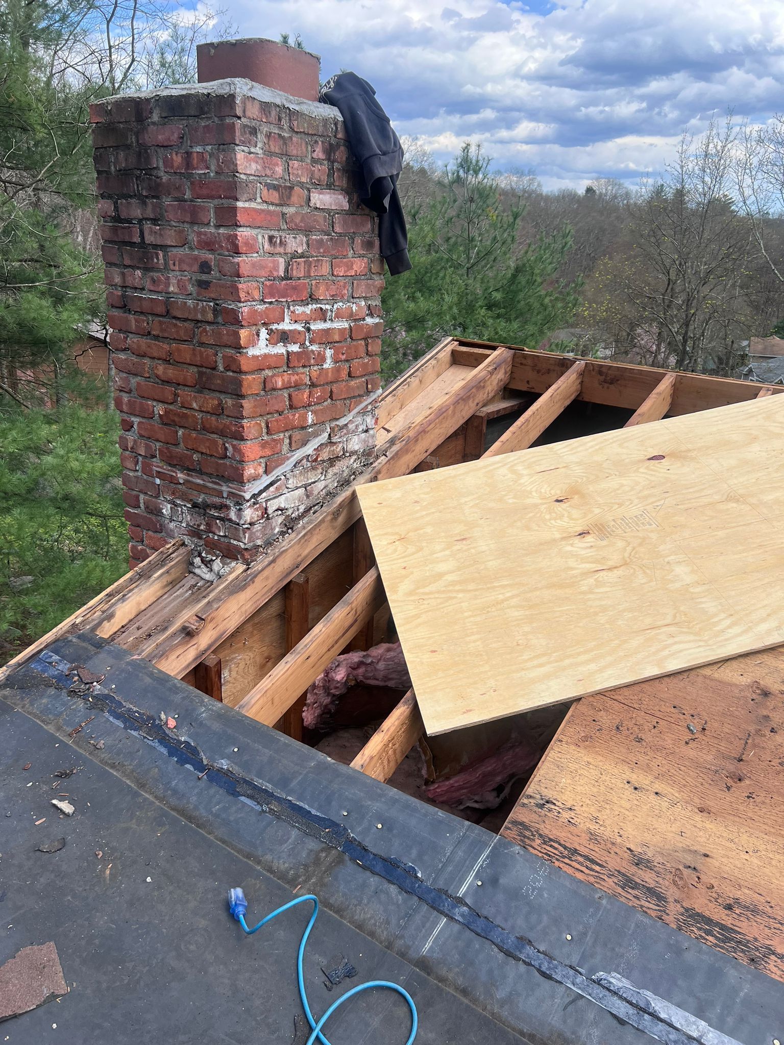 Chimney on a roof under repair; exposed wooden beams and plywood, blue sky background.
