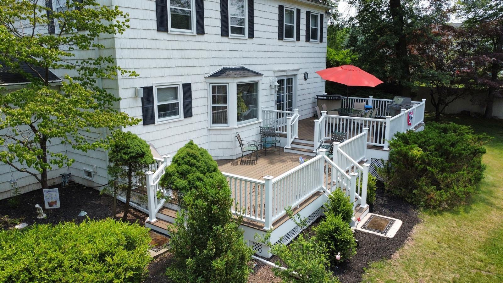 White house with a multi-level deck, red umbrella, and greenery in the yard.