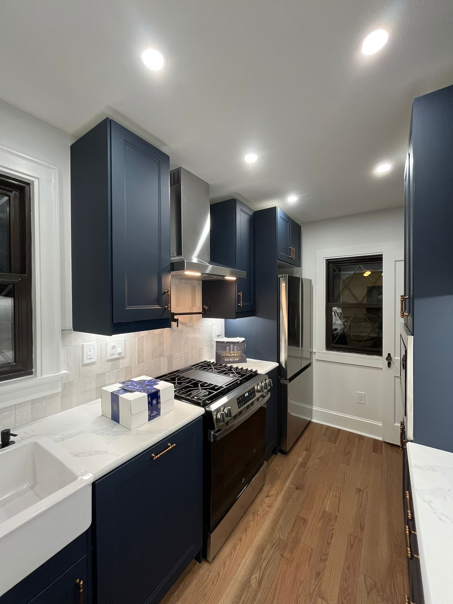 Navy blue kitchen with stainless steel appliances, white countertops, and wood floor.