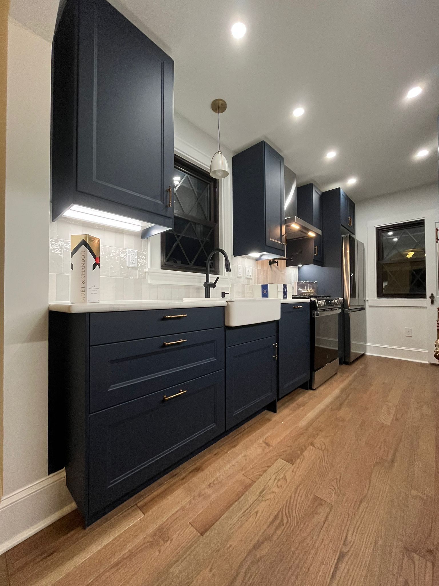 Navy kitchen cabinets, white sink, and stainless steel appliances. Hardwood floors.