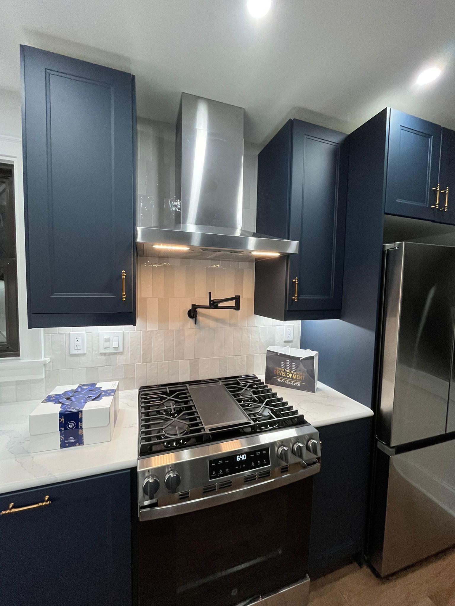 Modern kitchen with navy blue cabinets, stainless steel appliances, and white backsplash.