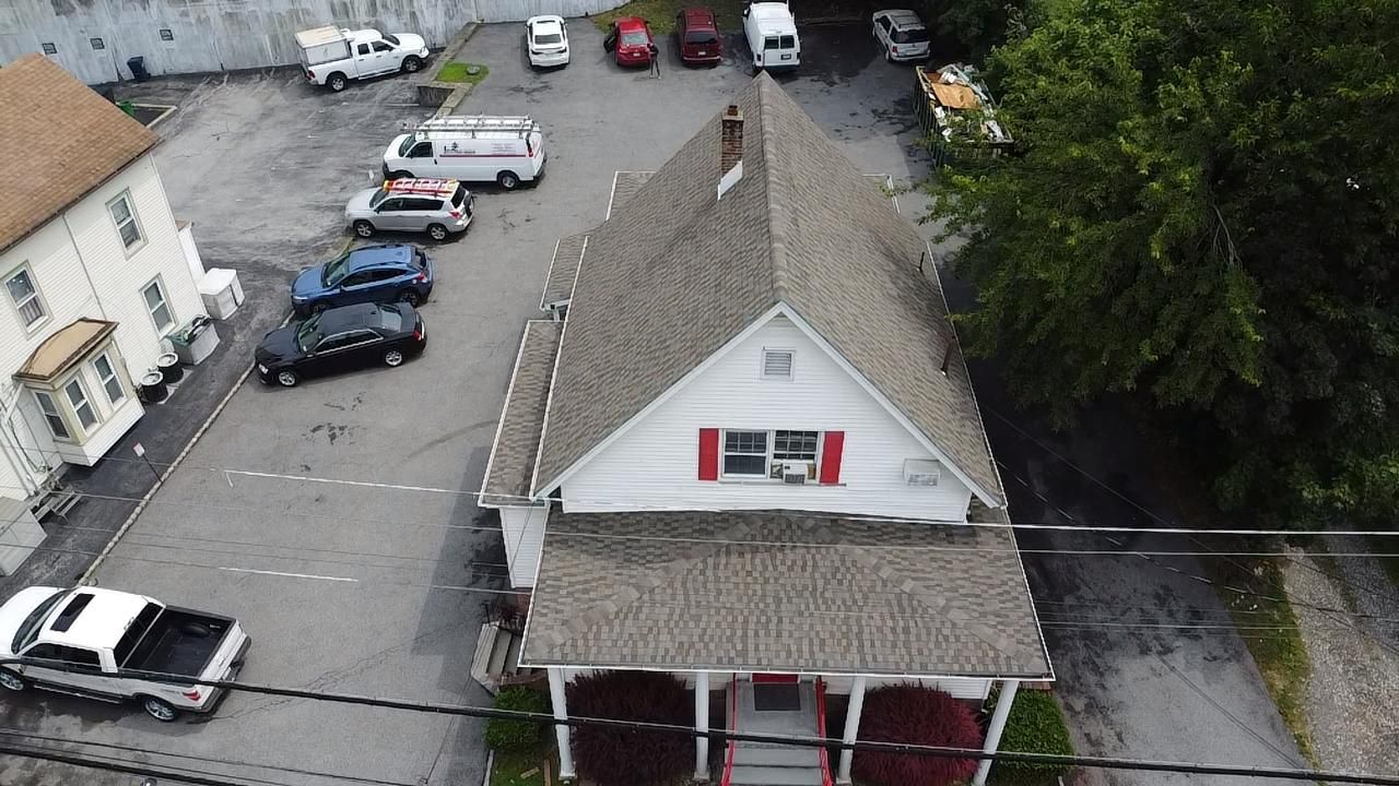 Bird's-eye view of a white building with red shutters. Cars parked around it in a parking lot.