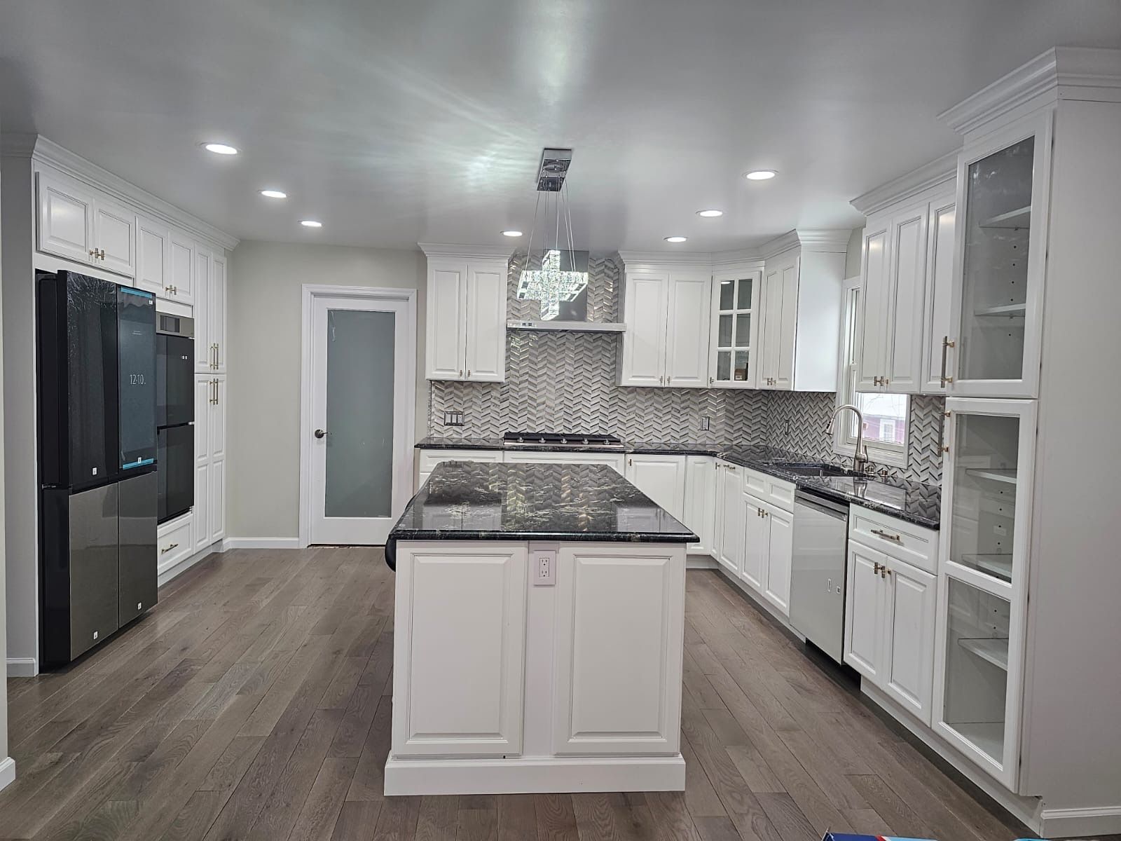 Bright white kitchen with island, cabinets, dark countertops, stainless steel appliances, and wooden floors.