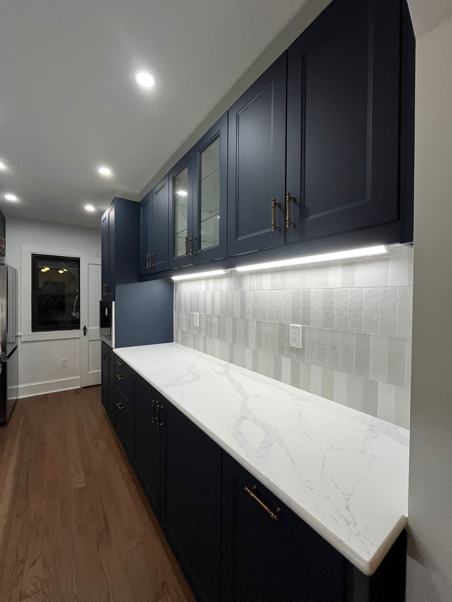 Navy blue kitchen cabinets with a white countertop and backsplash, under-cabinet lighting.