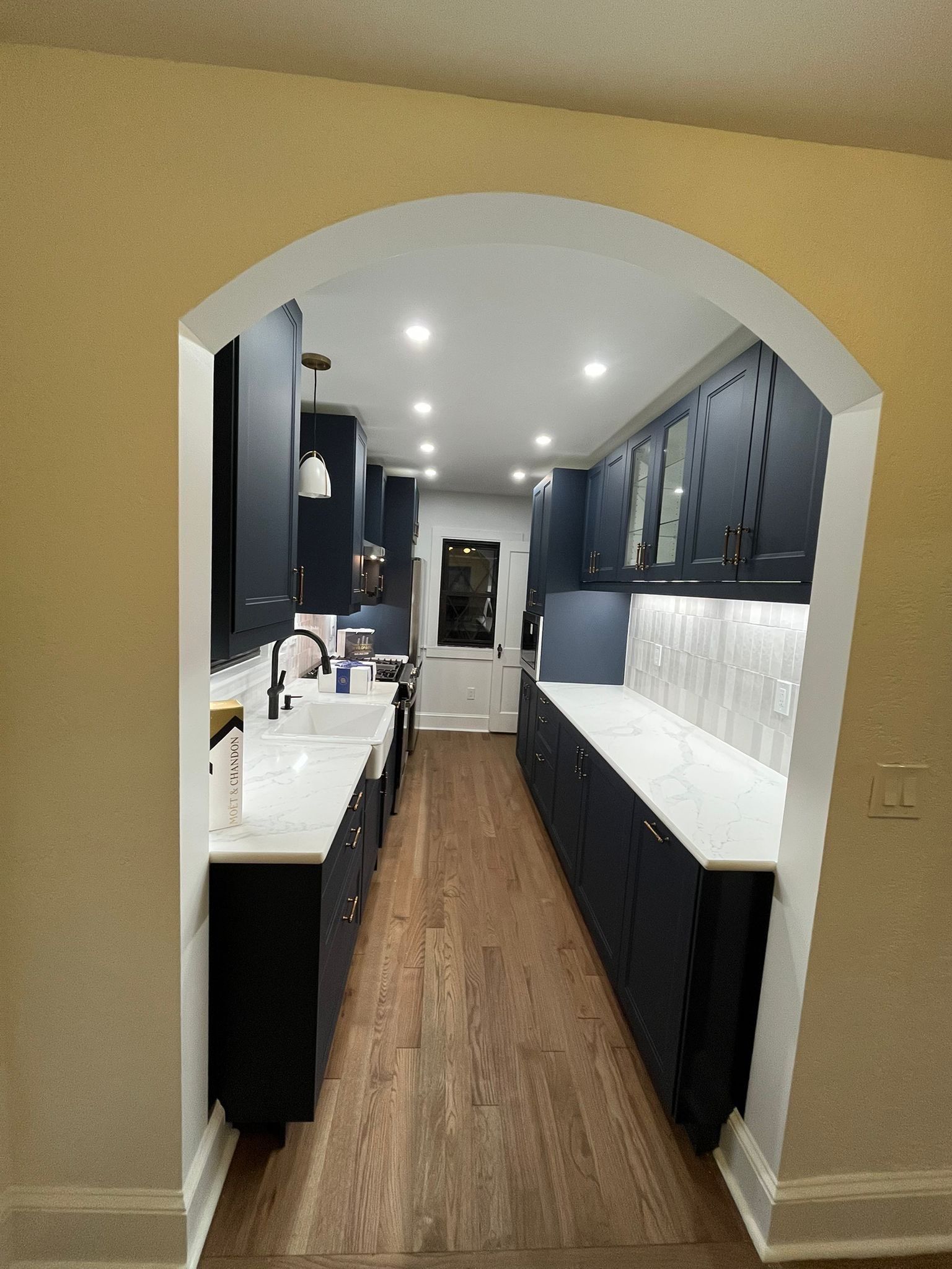 Navy blue kitchen with white countertops and wooden floor, seen through an arched doorway.