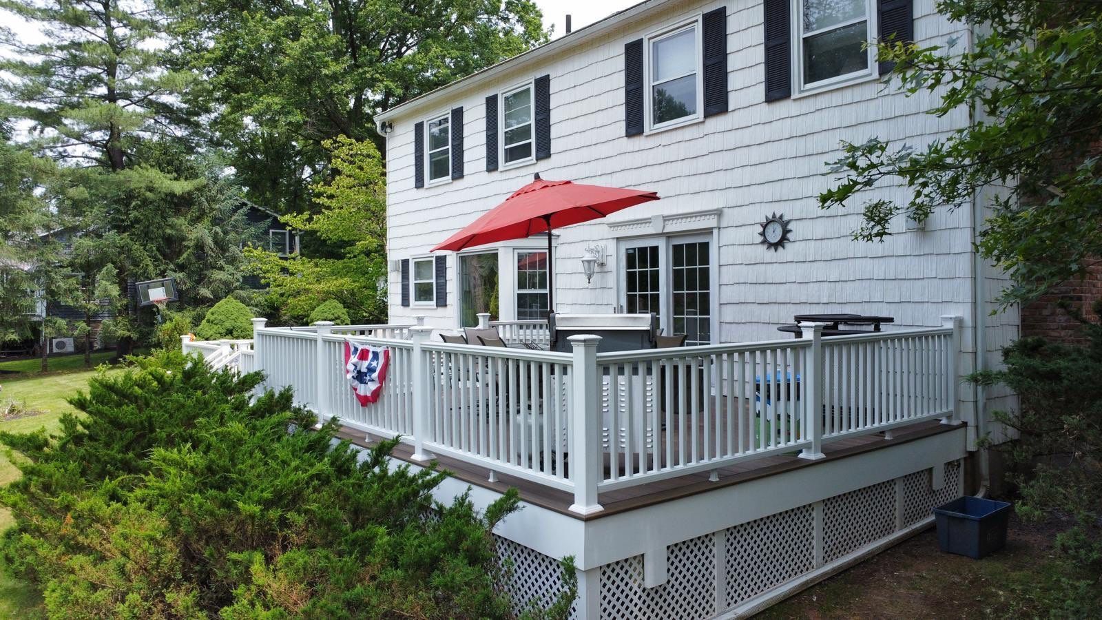 White house with a two-level deck; red umbrella, chairs, greenery, and American flag decorations.