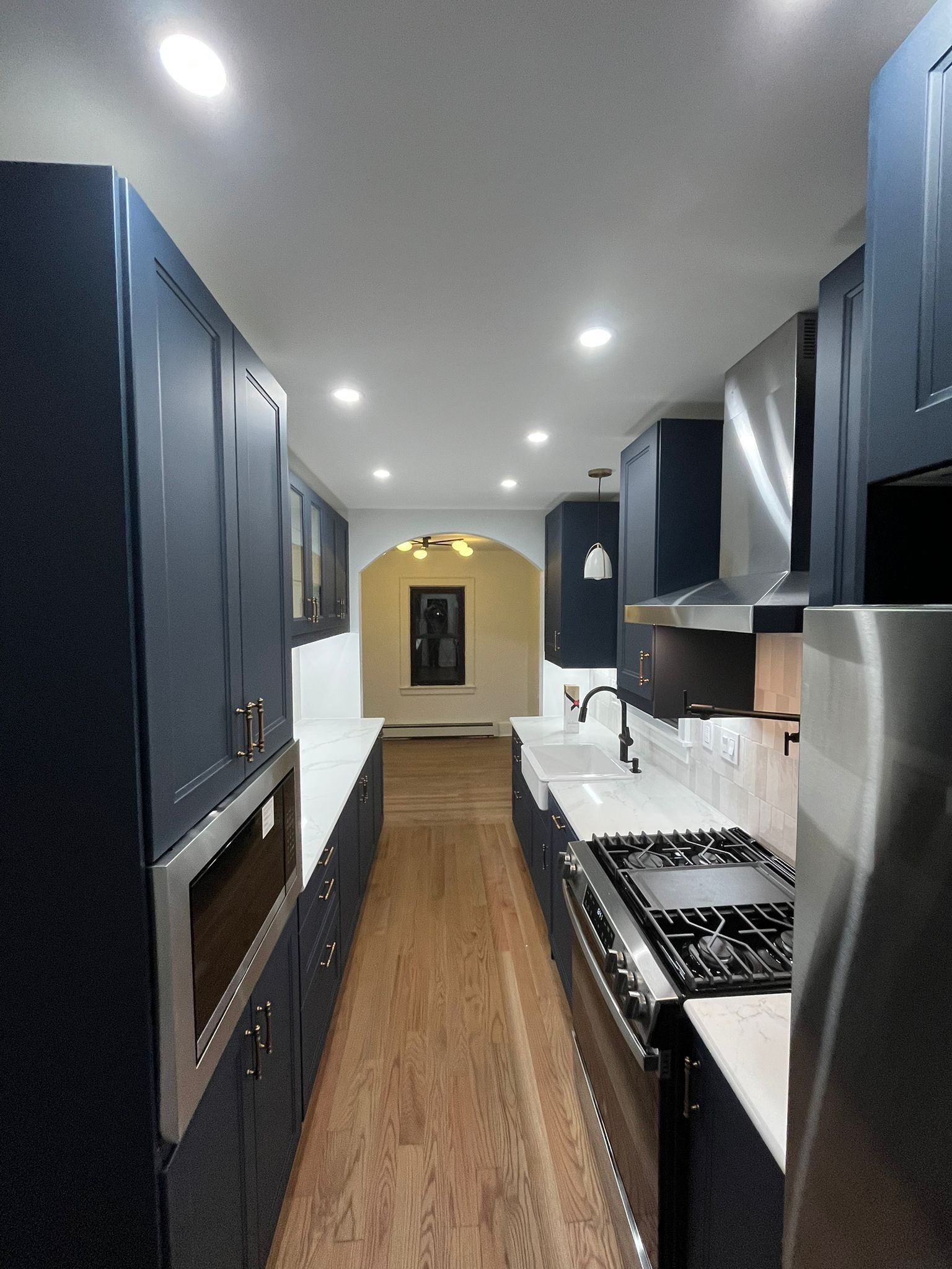 Navy kitchen with white countertops and stainless steel appliances. Hardwood floors lead to a doorway.