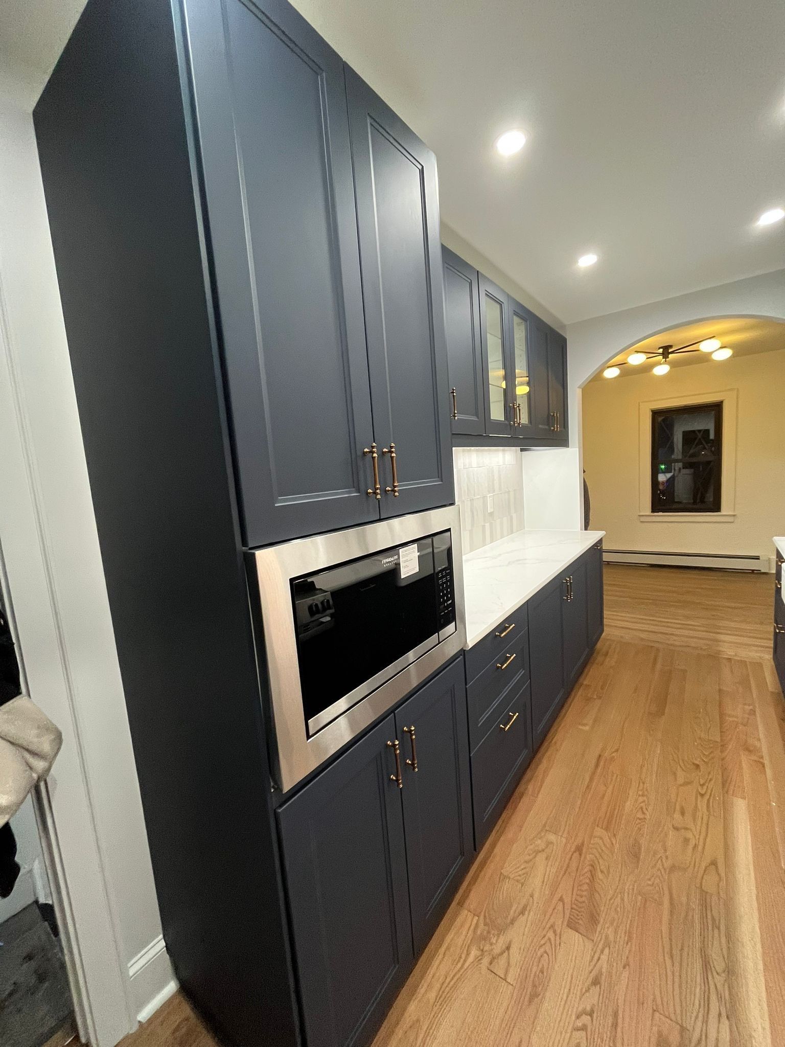 Dark blue kitchen cabinets with a built-in microwave and white countertops in a room with wood floors.