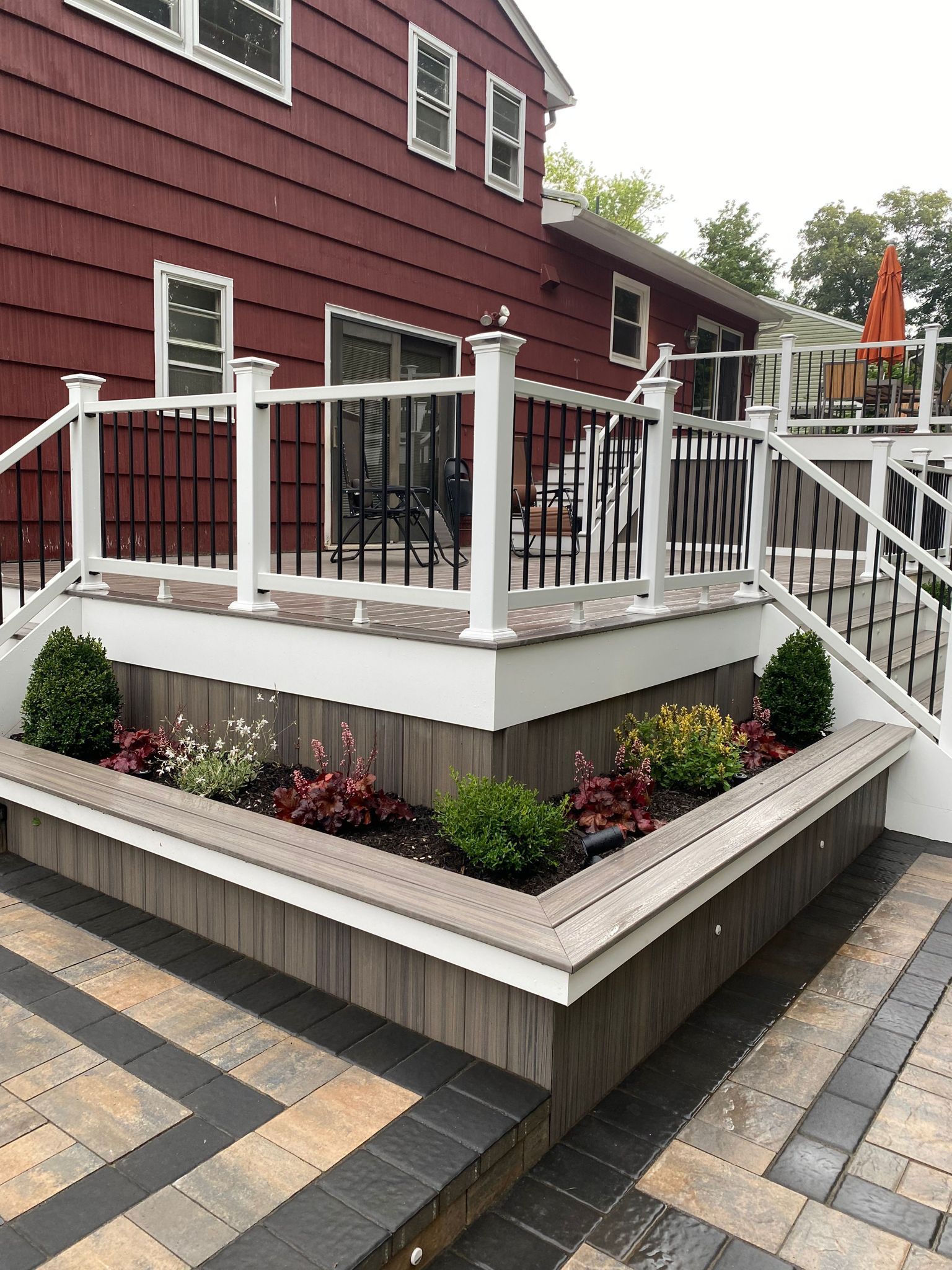 Wooden deck with railing, planters, and paver patio against a red house.