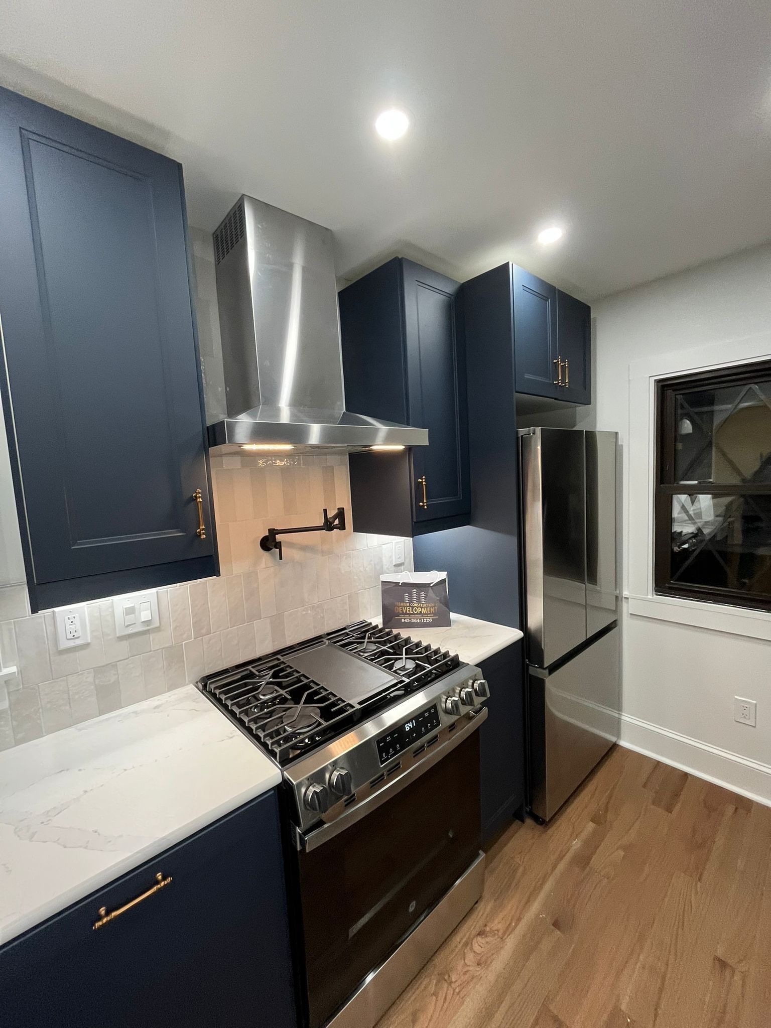 Dark blue kitchen with stainless steel appliances, white countertops, and wood floor.