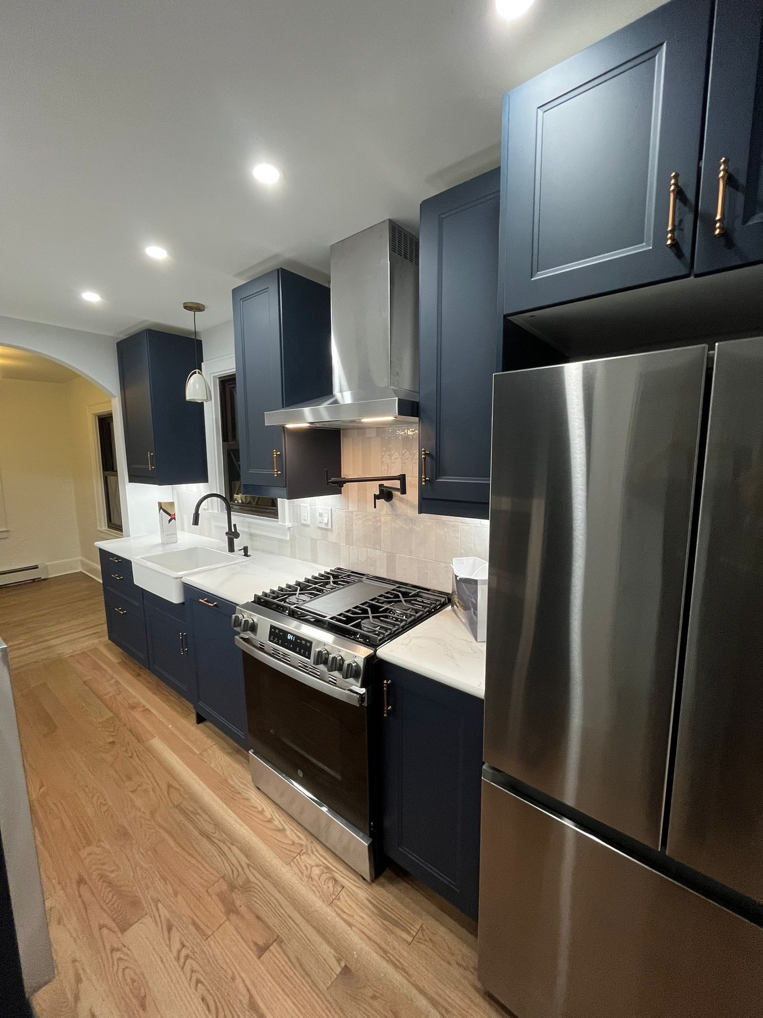 Navy blue kitchen with stainless steel appliances, white countertops, and wood floor.