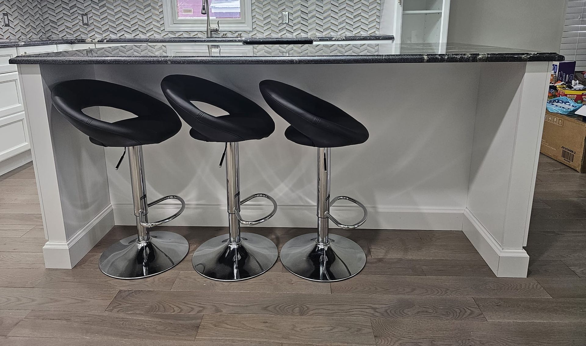 Kitchen island with three black stools and a dark countertop.