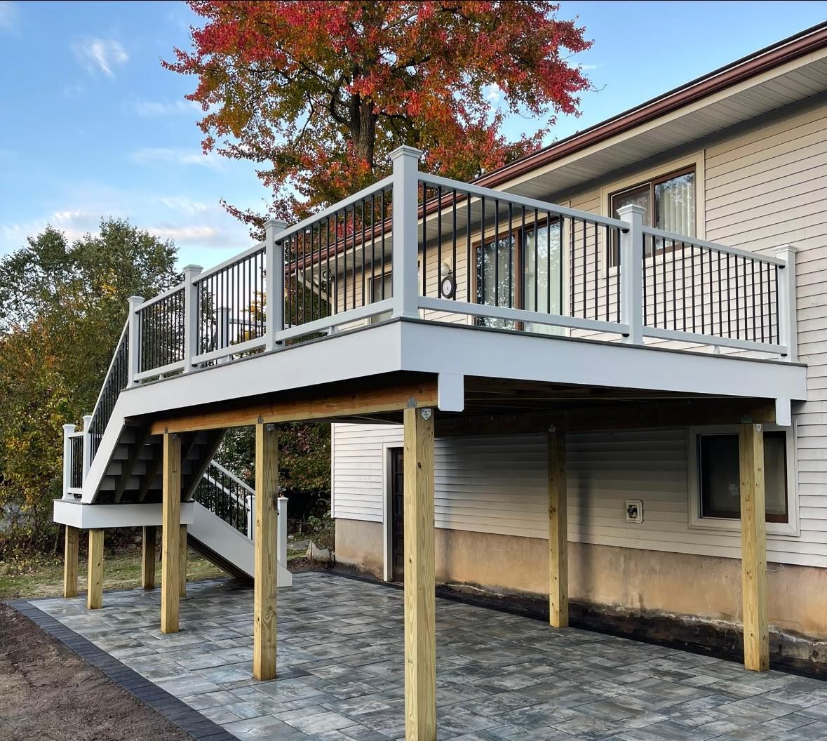 Gray and white elevated deck with black railing and stairs attached to a beige house, supported by wooden posts.