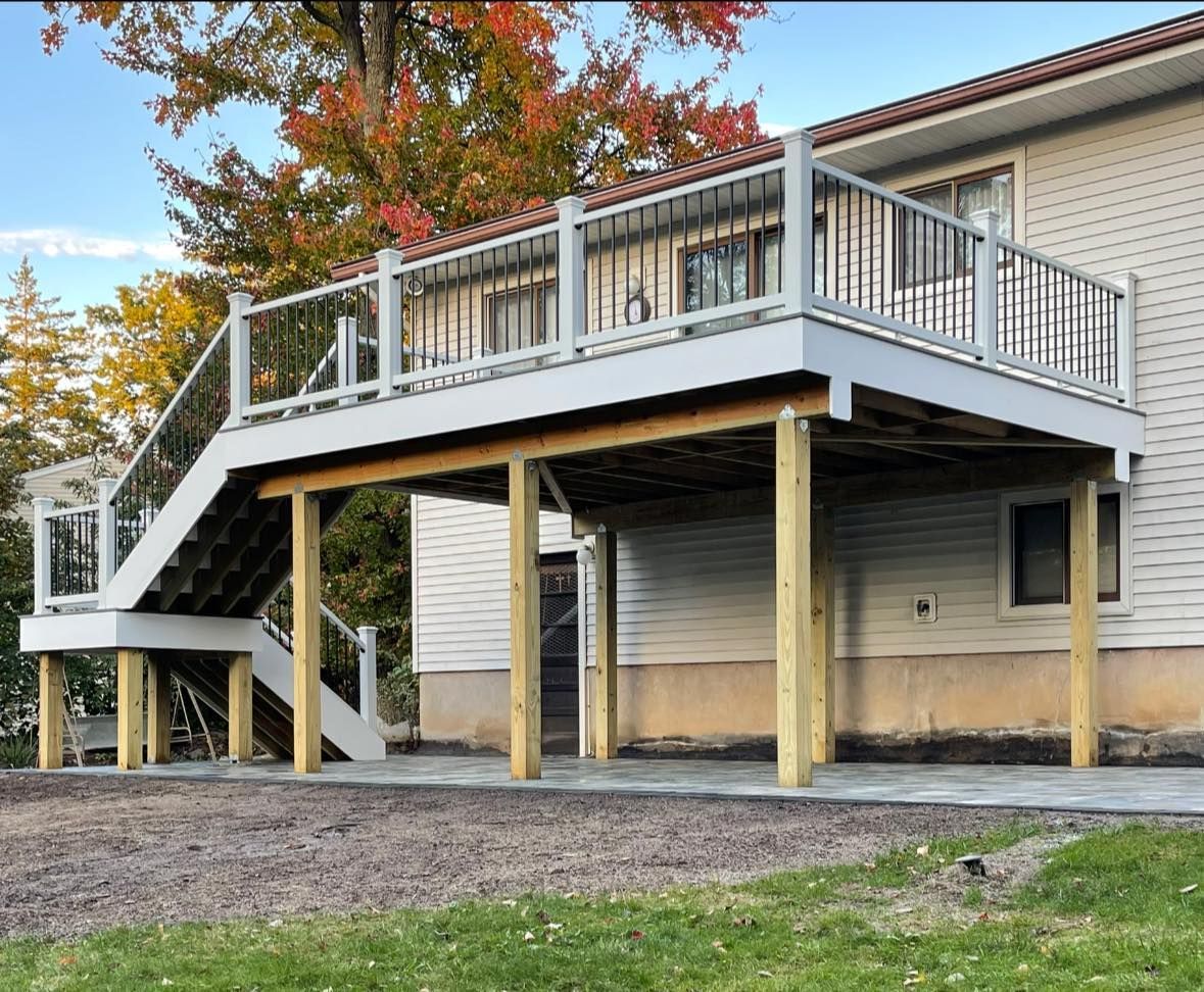 Elevated deck attached to a house with stairs and railings, supported by wooden posts, with a concrete patio below.