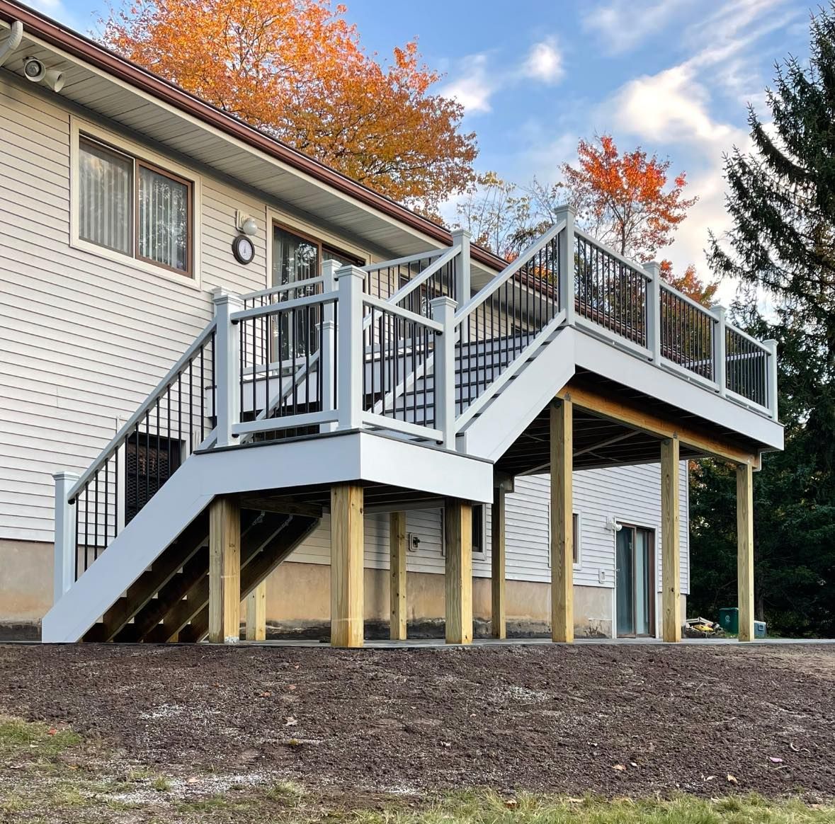 White deck with black railings and stairs attached to a house with fall foliage in the background.