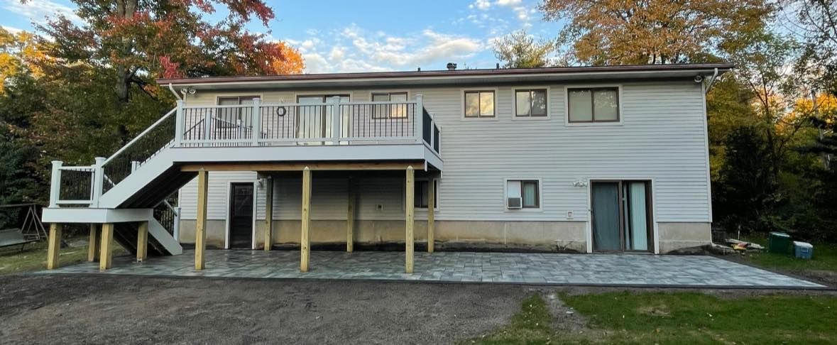 Back of a two-story white house with a deck and a paver patio in an autumn setting.