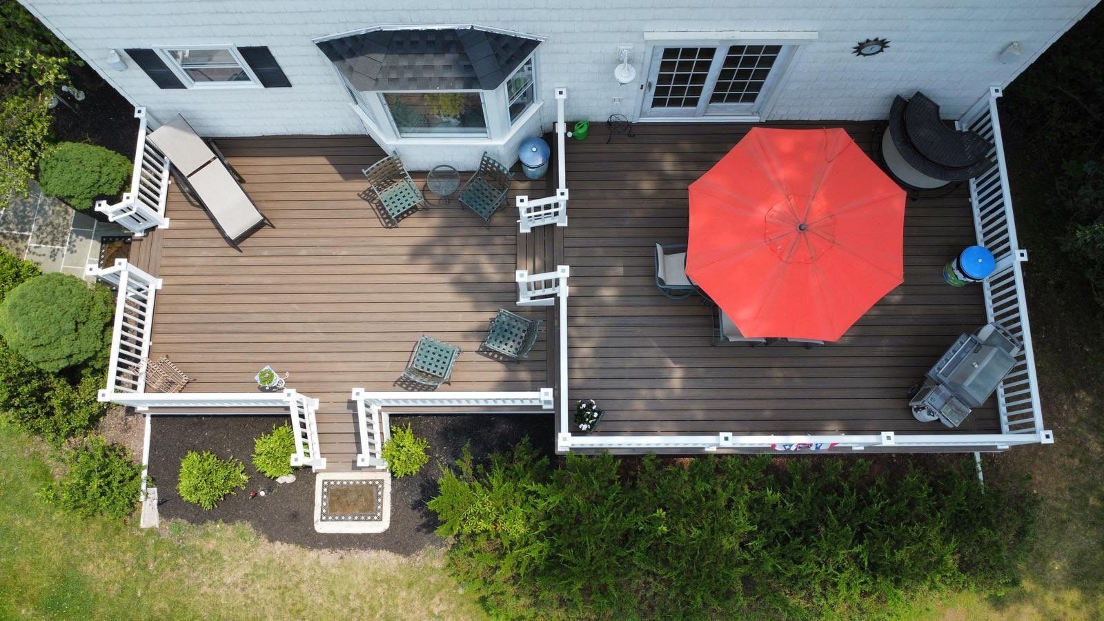Overhead view of a deck attached to a house with outdoor furniture, red umbrella, and shrubs.