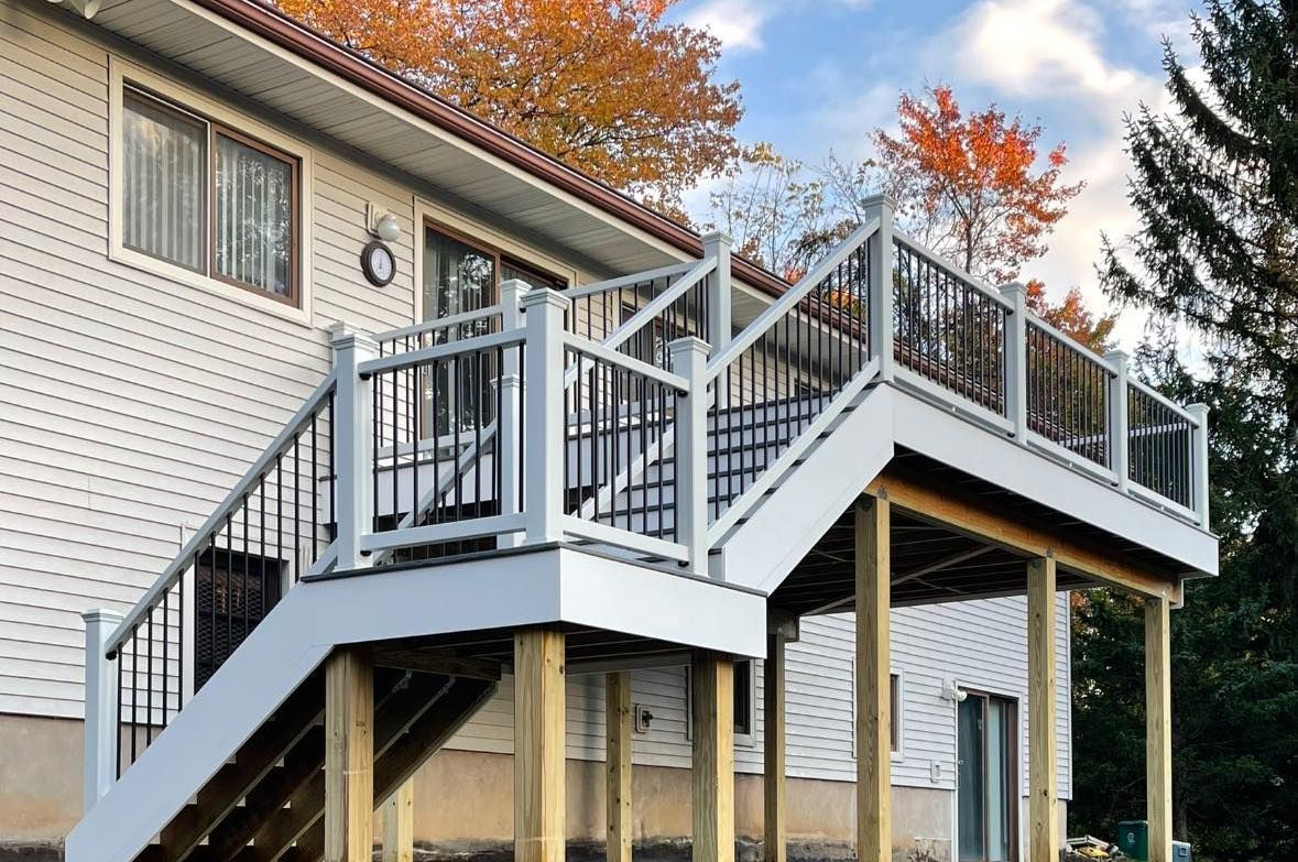 White and black deck with stairs attached to a two-story house, autumn trees in the background.