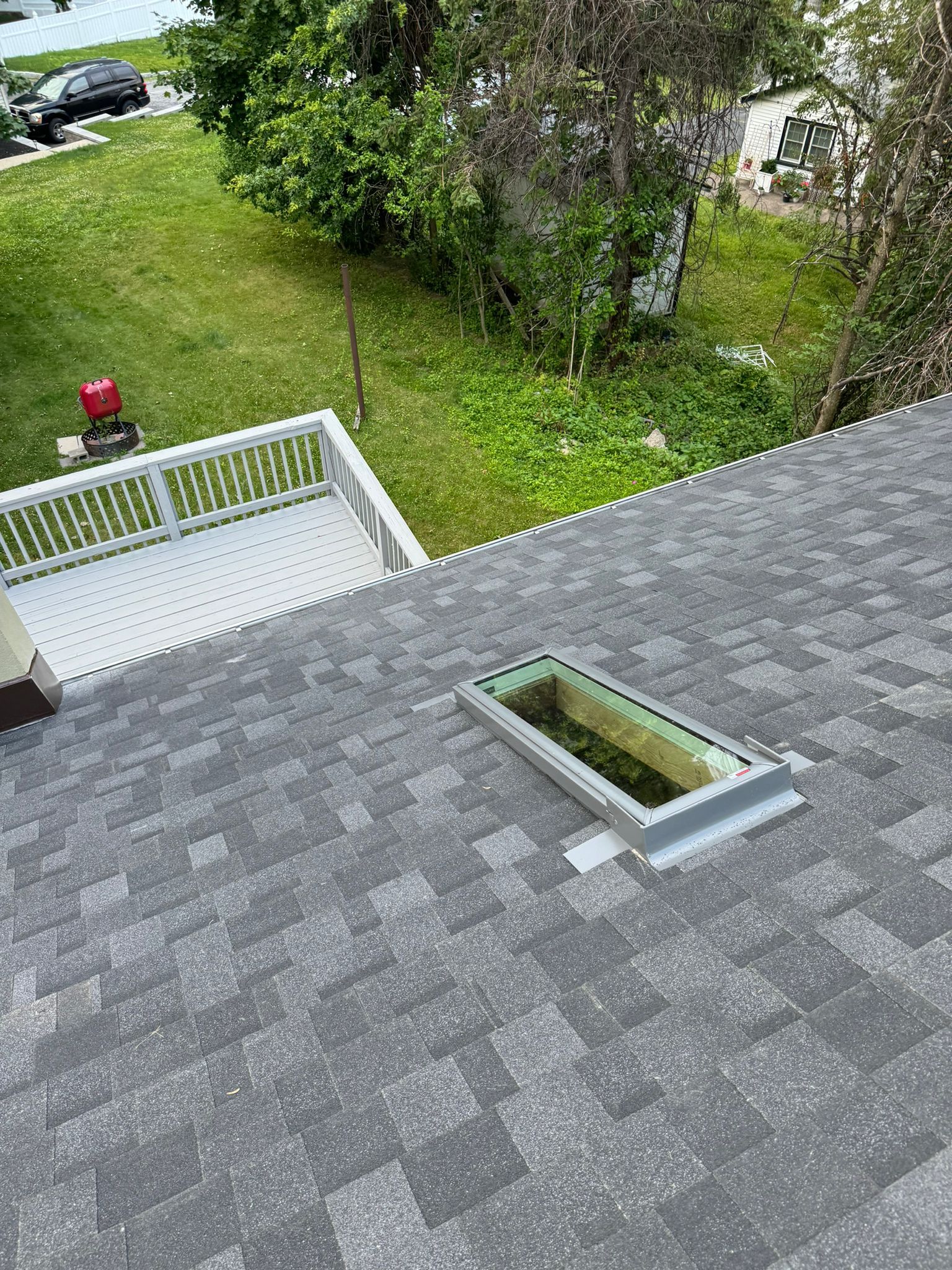 Gray asphalt shingle roof with a rectangular skylight. A white deck and green yard are in the background.