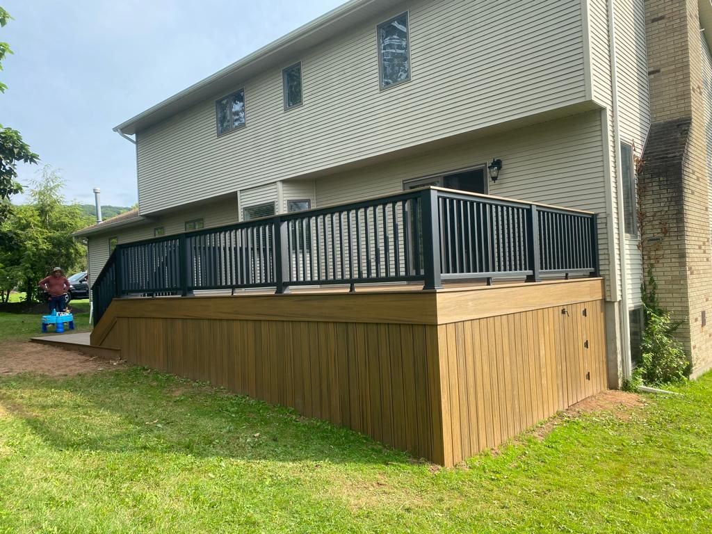 Deck attached to a two-story house with dark railings and brown siding.
