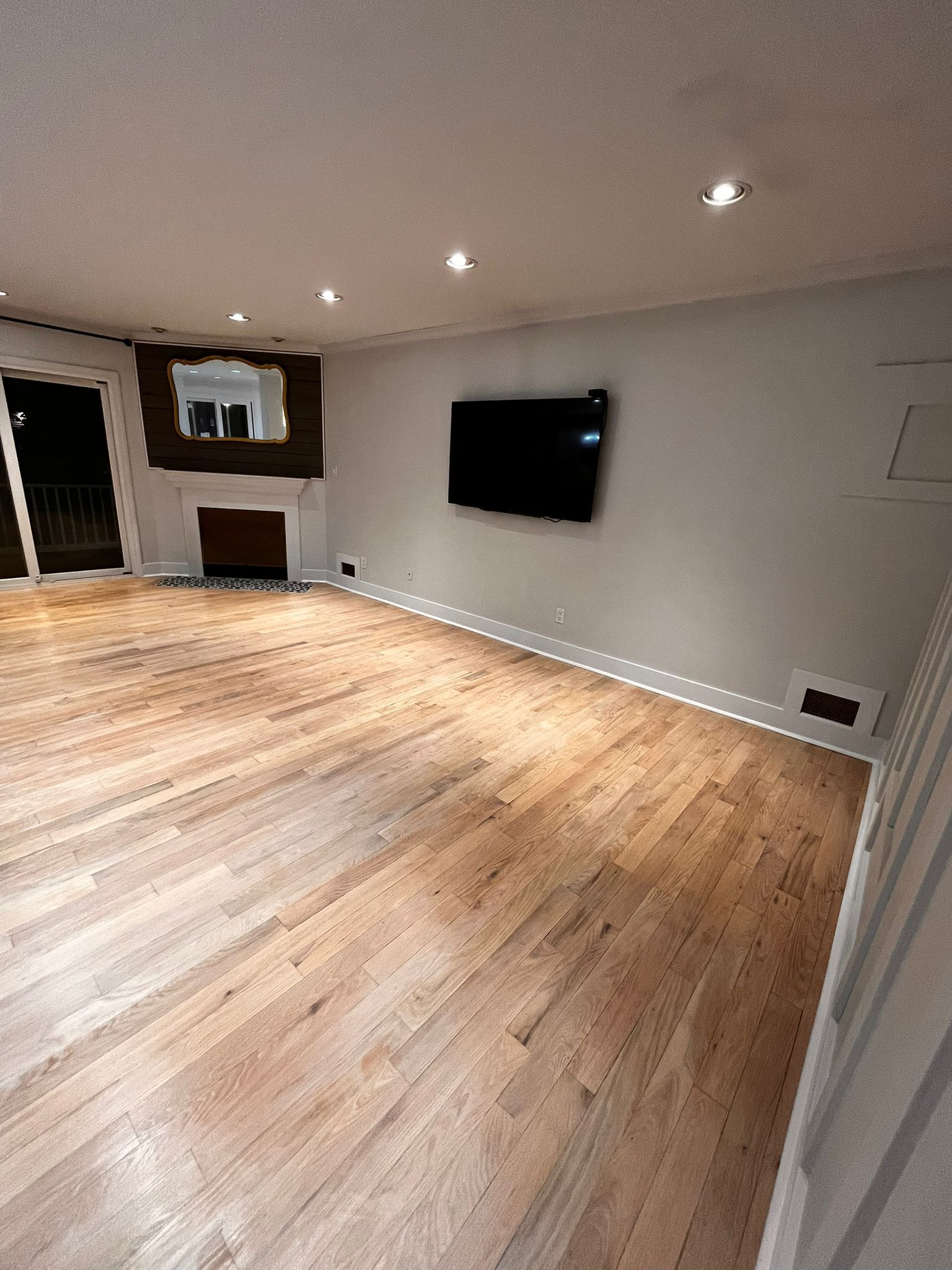 Empty living room with wood floor, TV, fireplace, and white walls.