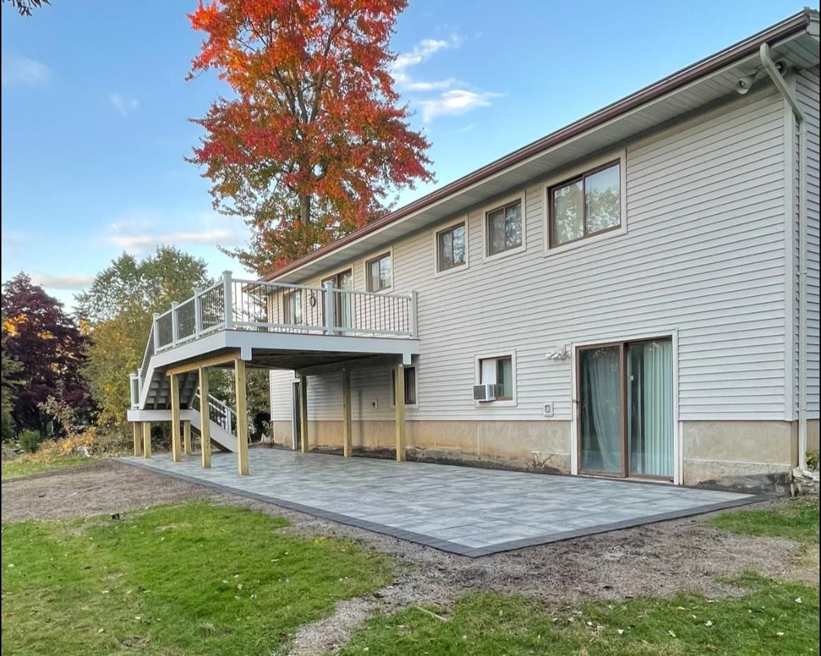 House with a gray deck, patio, and siding. Fall foliage and blue sky in the background.