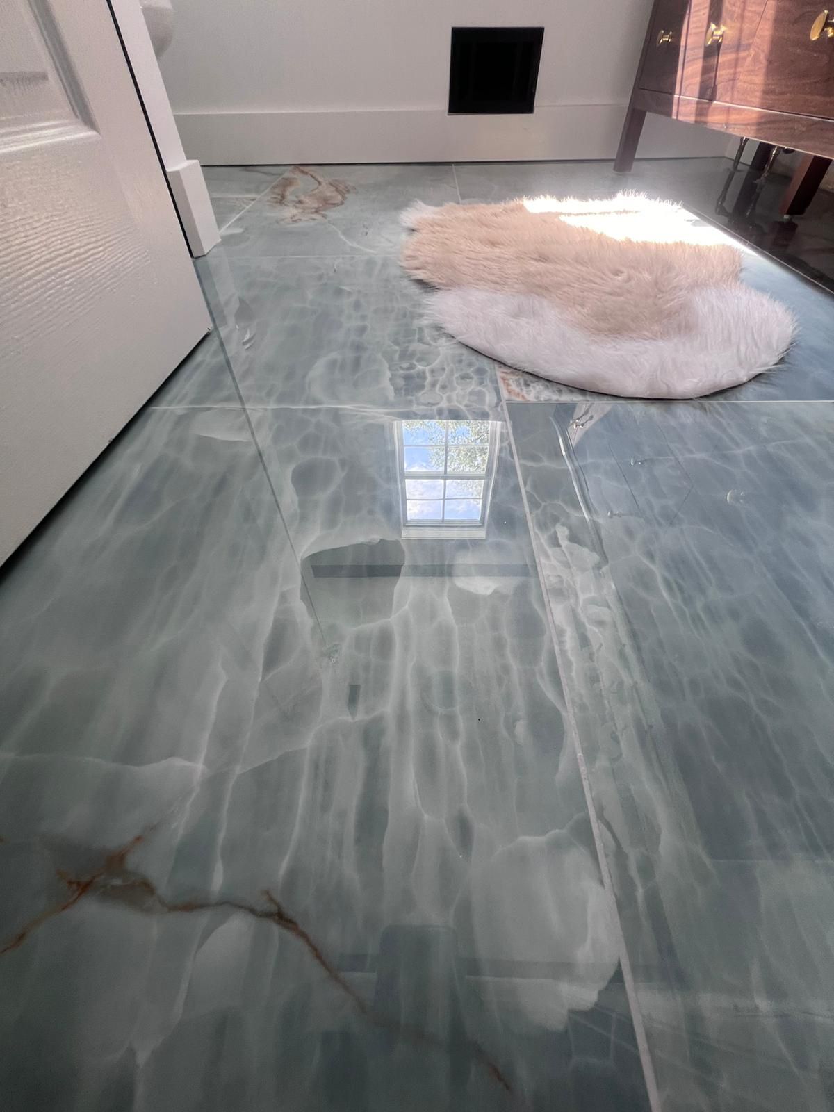 Blue-green stone tile floor with a white fluffy rug.  A window reflects light, and there is a door on the left.