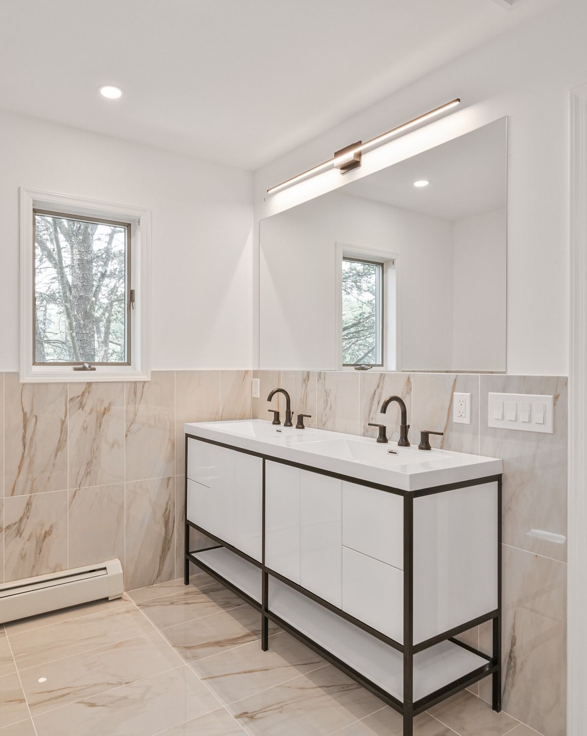 Modern bathroom with white vanity, black hardware, large mirror, and marble-look tile.