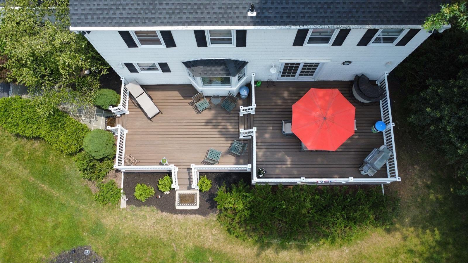 Overhead view of a two-story house with a wooden deck featuring a red umbrella, chairs, and a small garden.