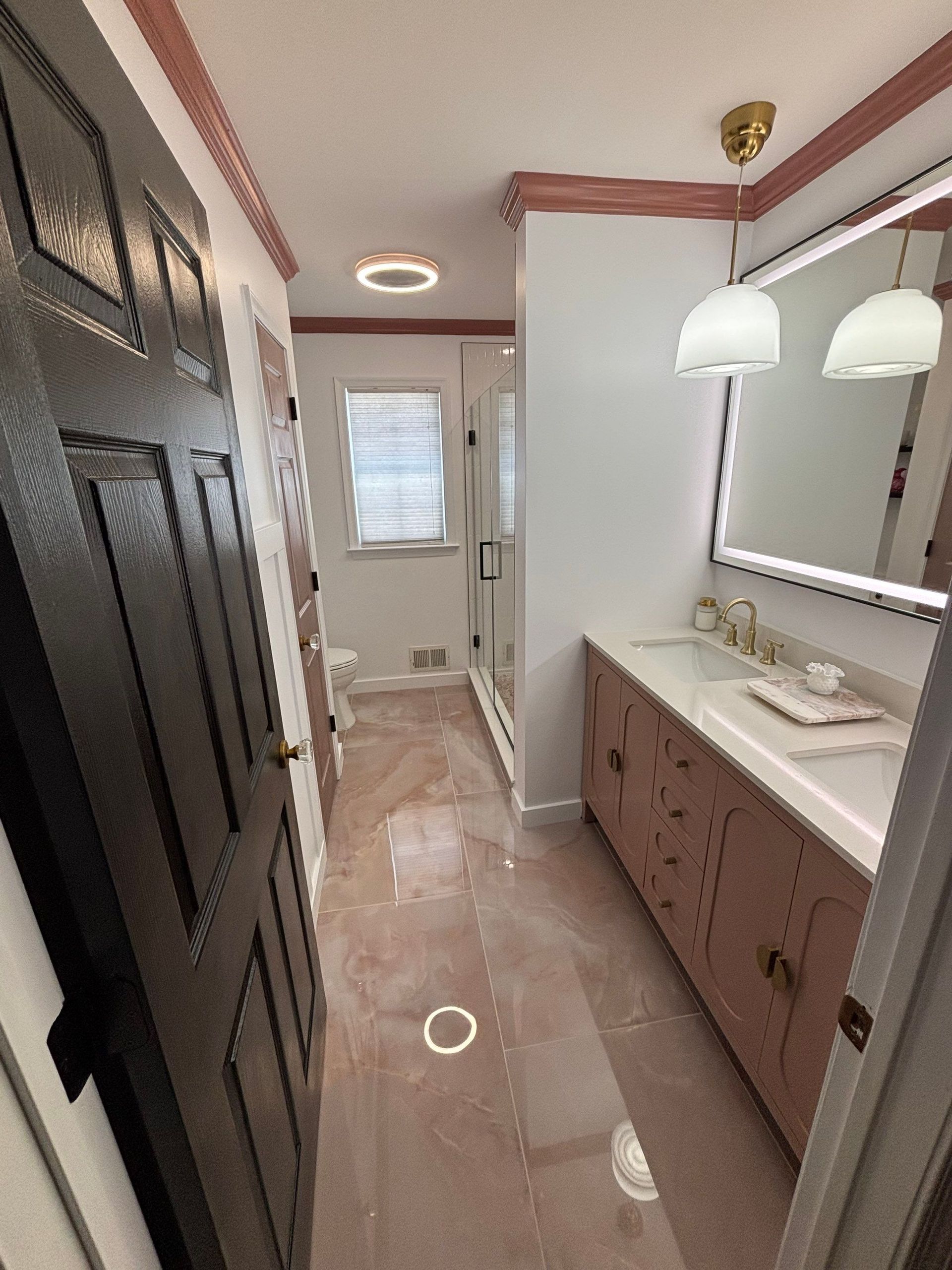 Bathroom with pink floor, vanity, and trim; black door on left, shower and window at the end.
