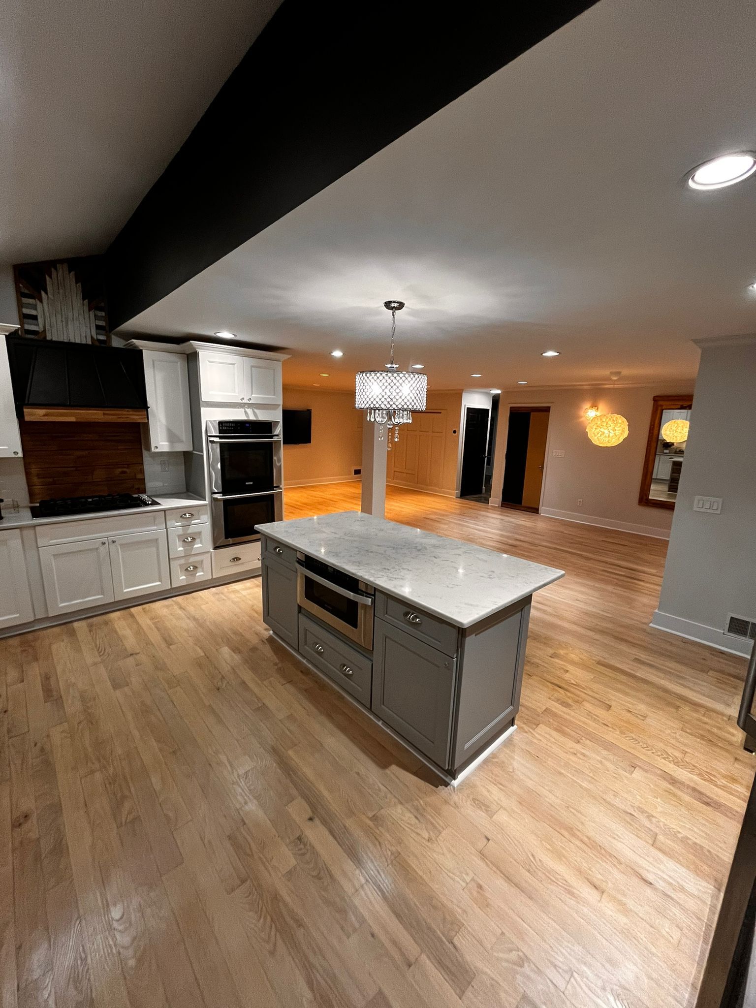 Kitchen with gray island, light cabinets, wooden floors, and view into living area.