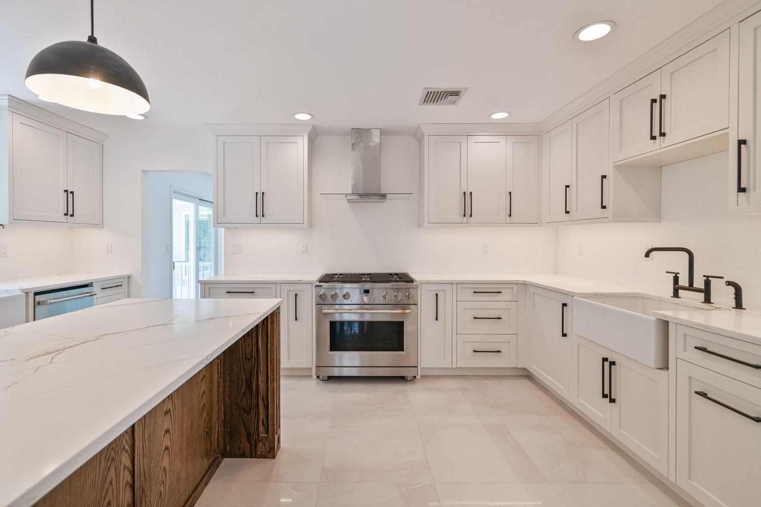 Modern white kitchen with stainless steel appliances, white countertops, and wood island.