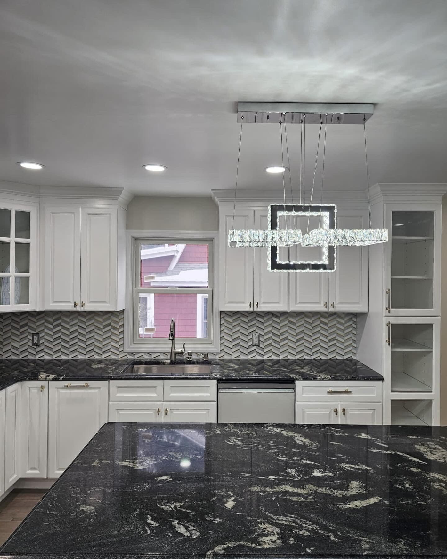 White kitchen with black granite countertops, mosaic backsplash, and modern chandelier.